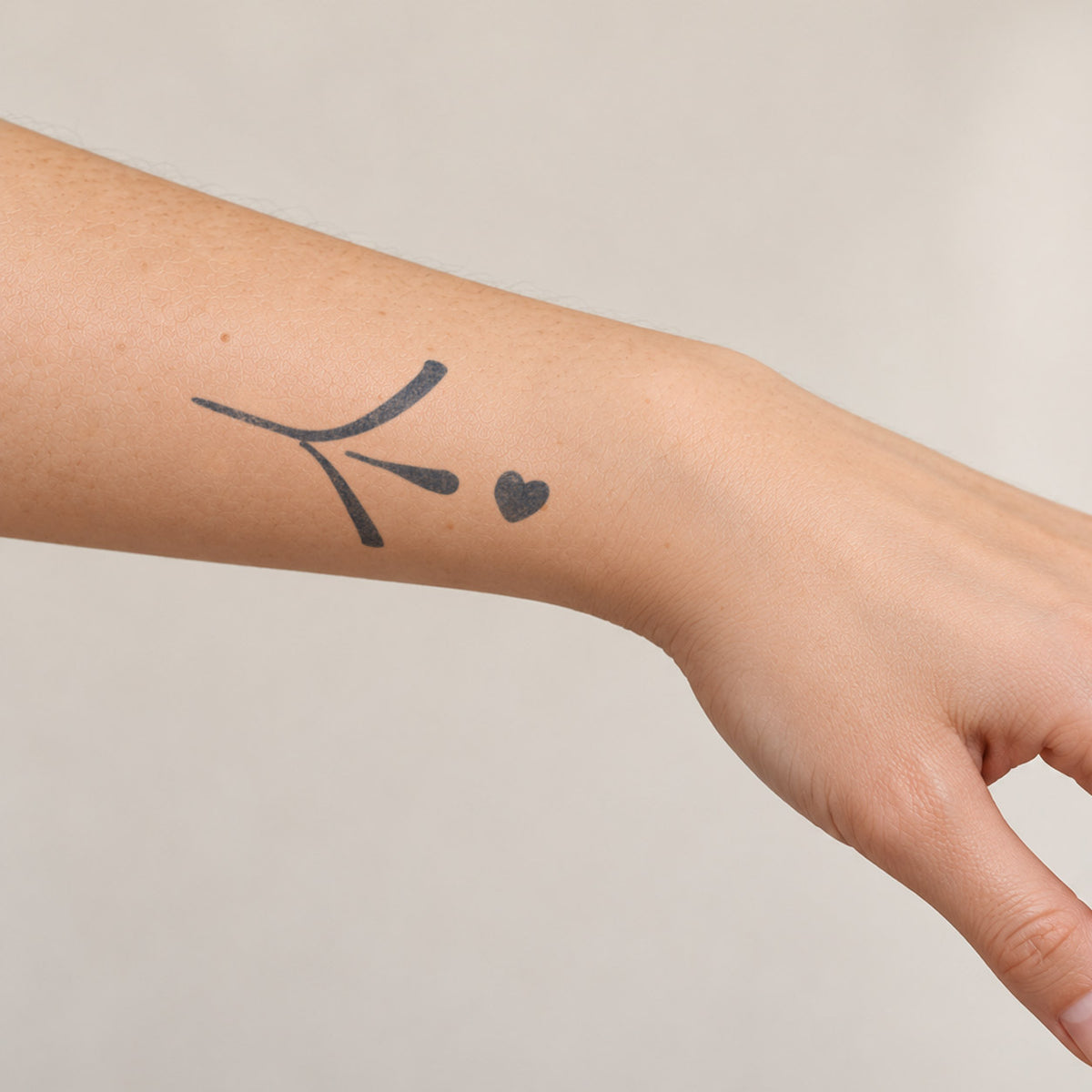 Small temporary tattoos featuring an abstract line symbol paired with a small heart in blue-black ink near the wrist.