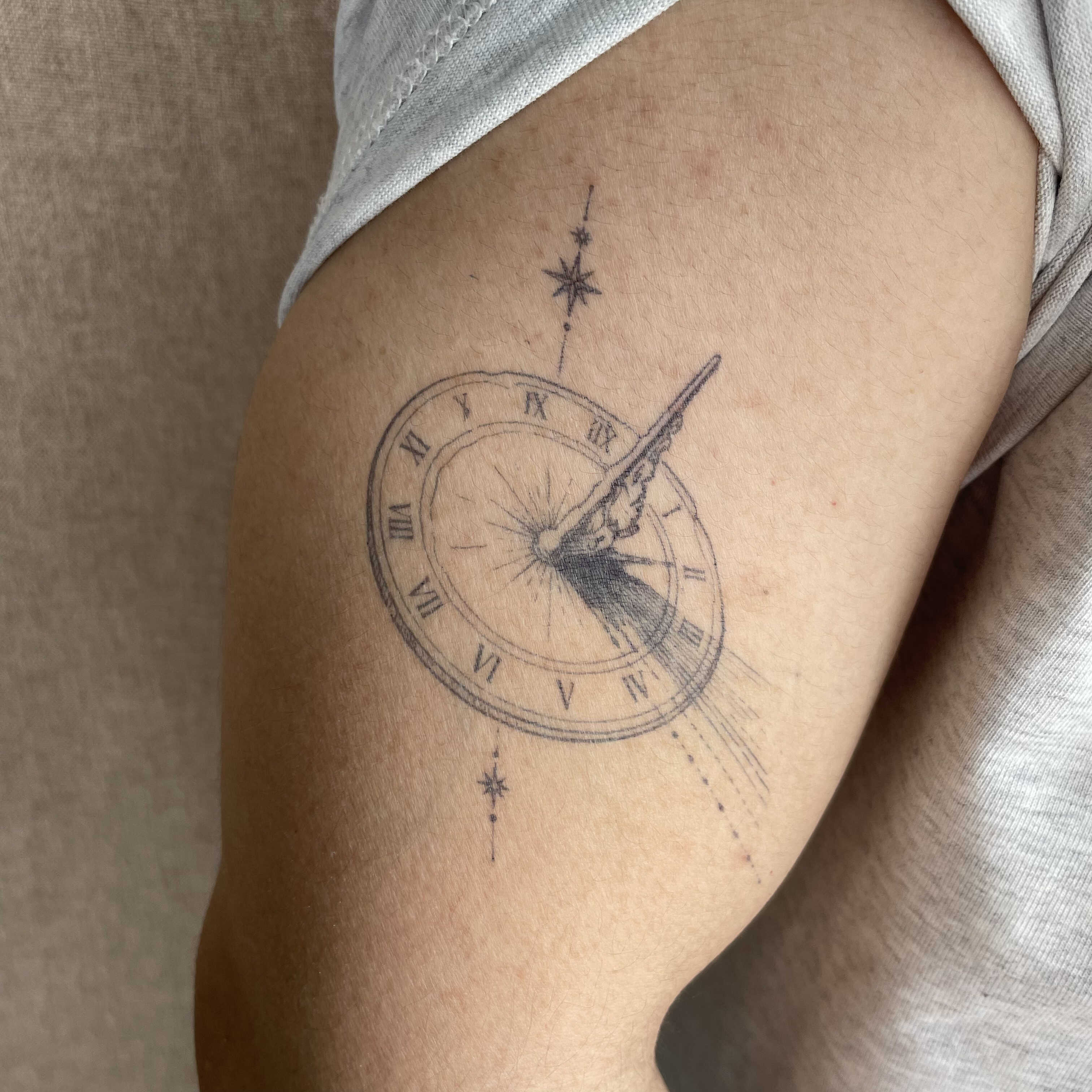 Minimalist sundial semi-permanent tattoo on the upper arm.