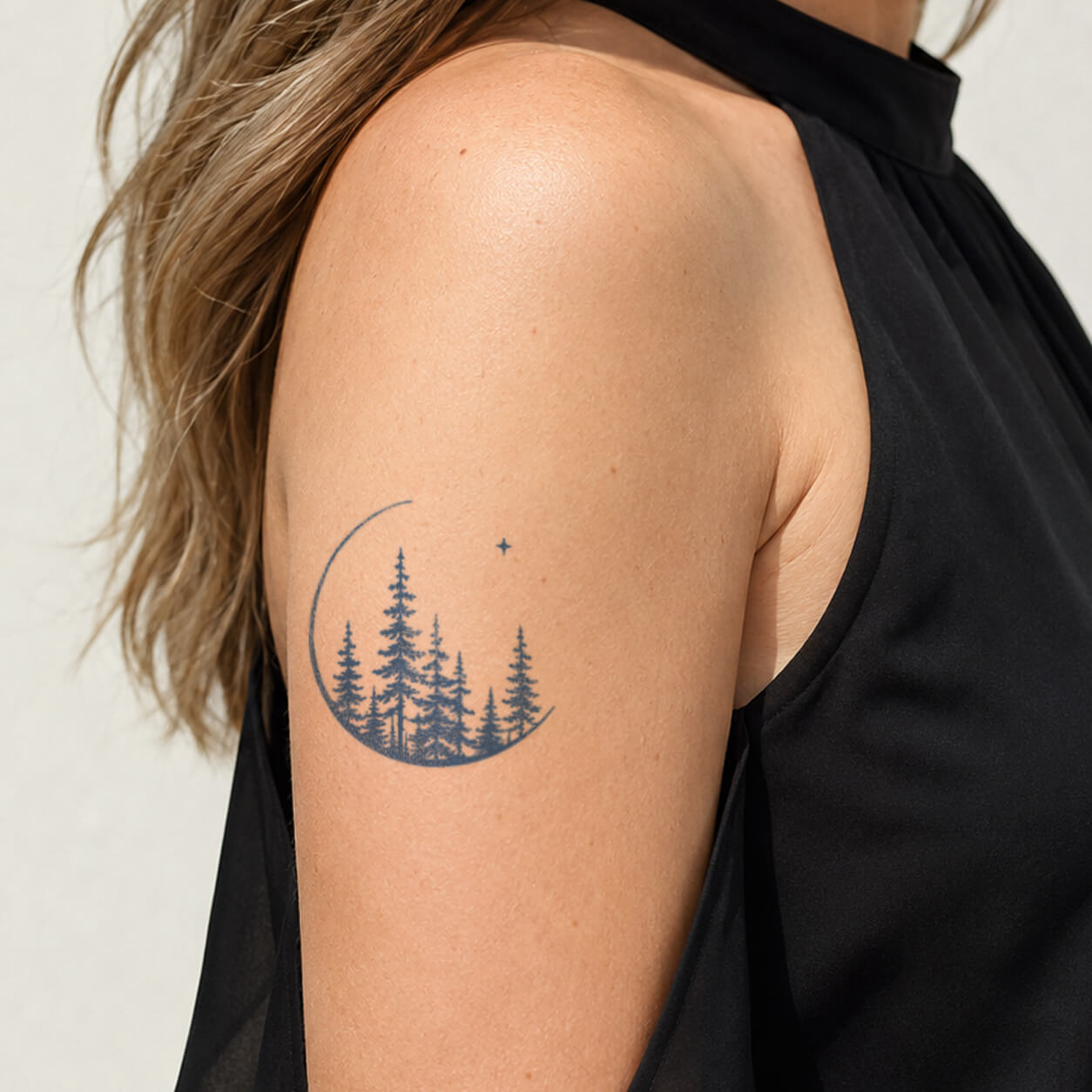 Minimal moon and pine forest temporary tattoo featuring a crescent moon, evergreen trees, and small stars in a nature-inspired landscape design on the upper arm