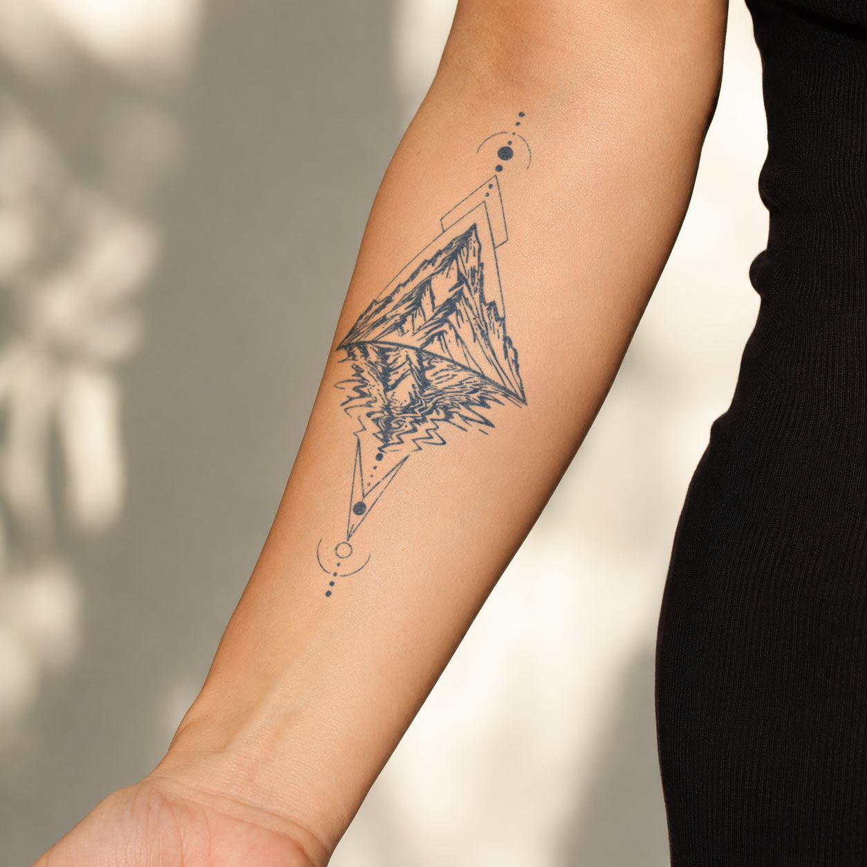 Temporary forearm tattoos featuring mountain peaks reflected in water with geometric triangles and celestial orbit details.