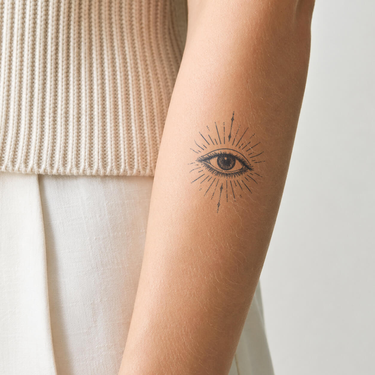 Delicate fine line tattoo featuring a detailed eye surrounded by radiant sunburst rays and small celestial accents. This minimalist temporary tattoo design combines a mystical eye symbol with elegant linework for a unique and artistic look.