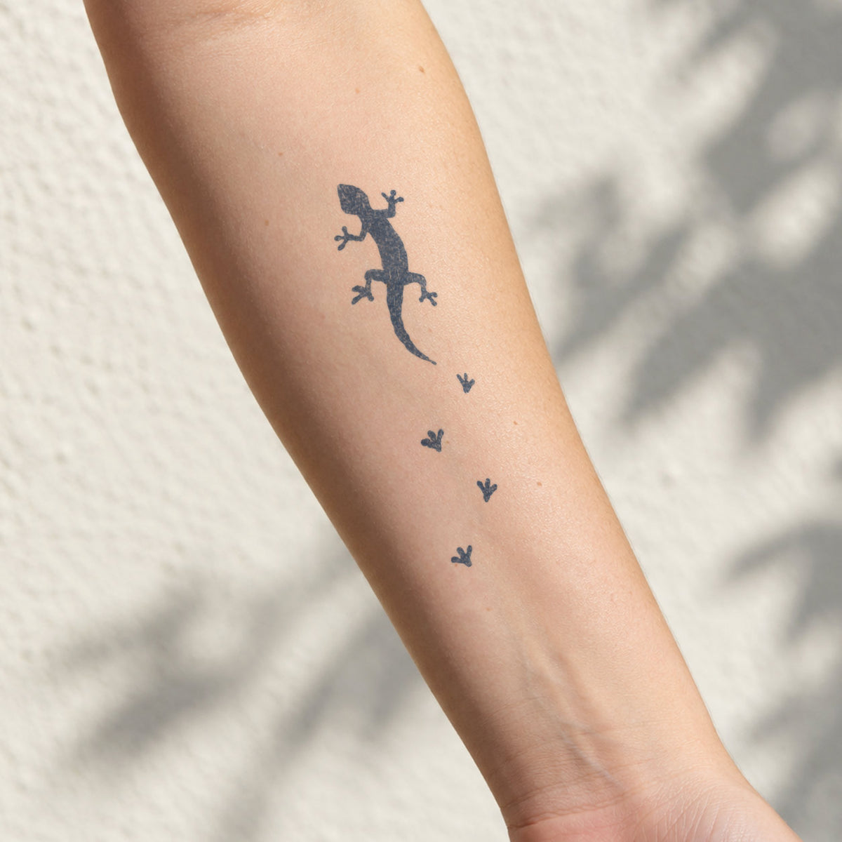 Temporary forearm tattoos featuring a minimalist lizard with small footprints in a blue-black design on the inner forearm.