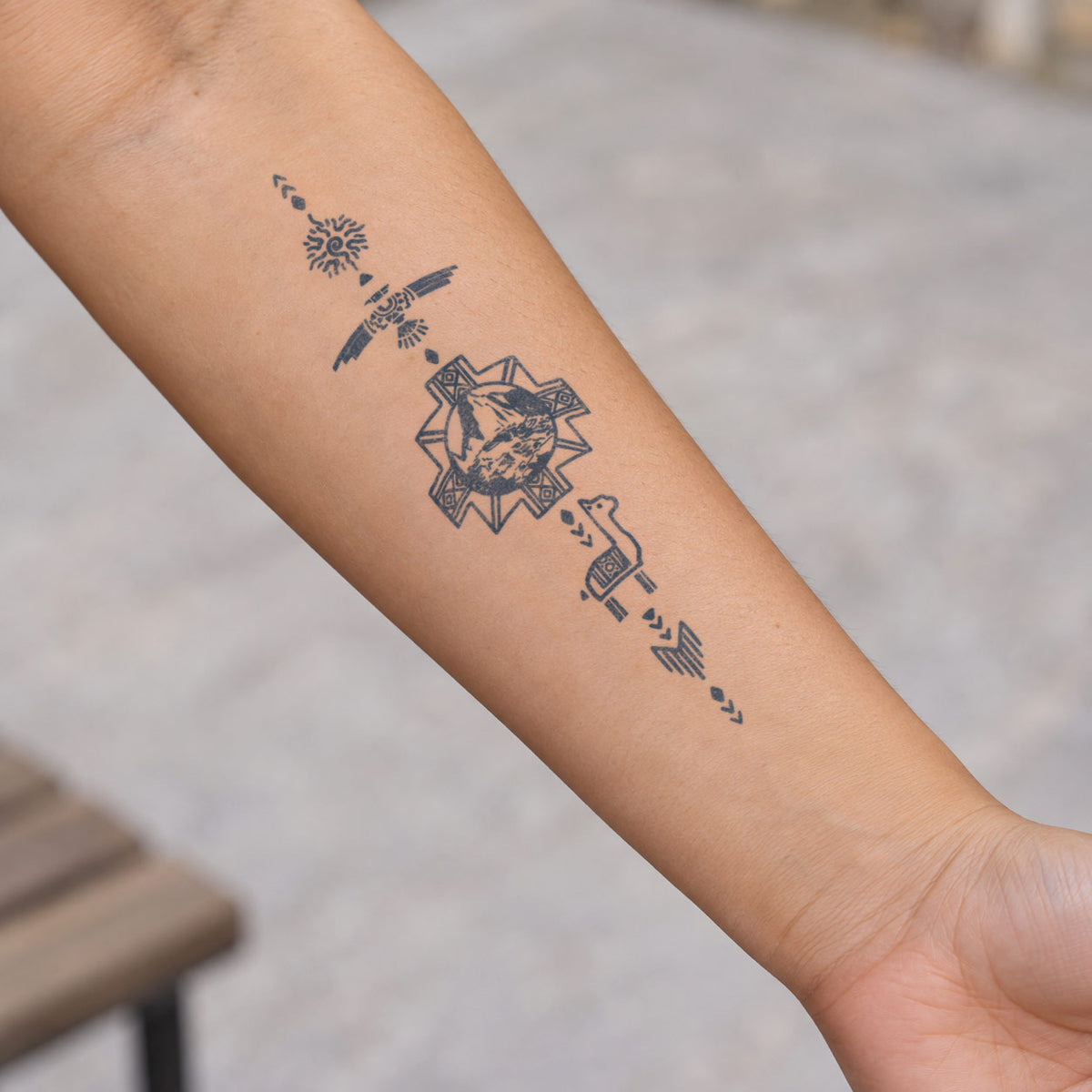Art temporary tattoos featuring a mountain landscape, flying bird, sun, and nature-inspired geometric symbols in blue-black ink on the forearm.