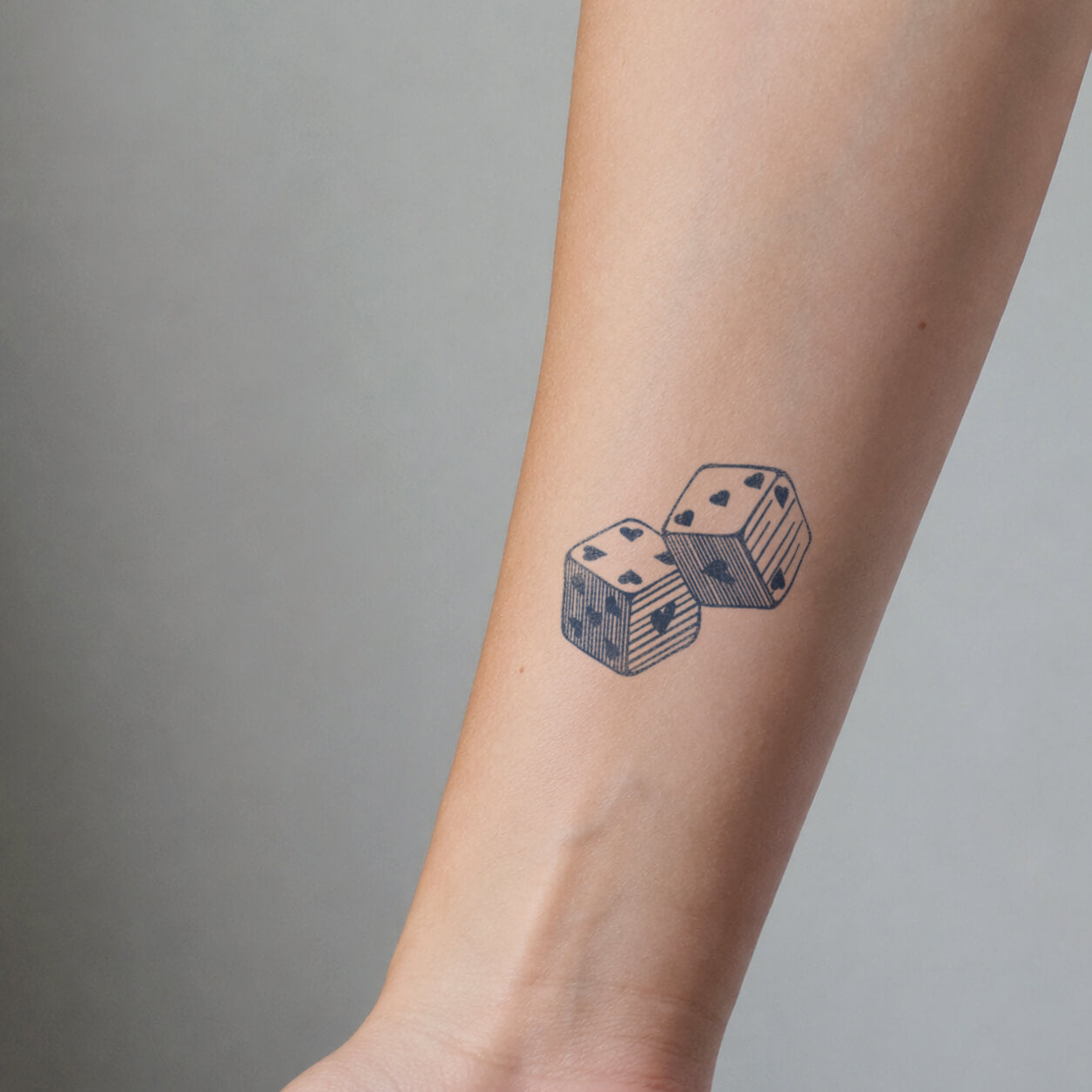 Minimalist tattoo featuring two detailed dice with heart-shaped pips and vintage engraving-style linework. This small temporary tattoo design represents luck, chance, and playful energy with a classic casino-inspired style.