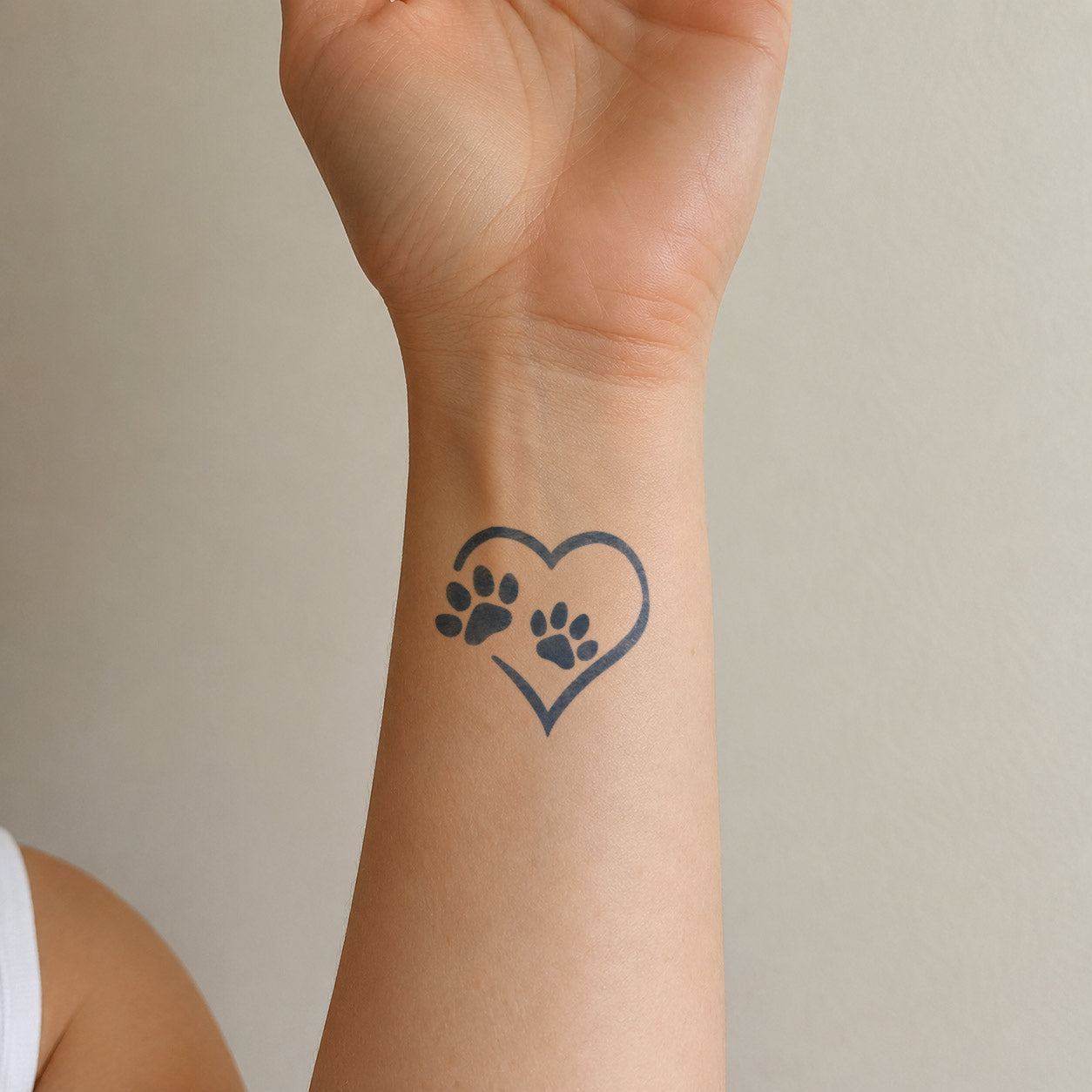 Small temporary tattoos featuring two black paw prints inside a simple heart outline on the wrist.
