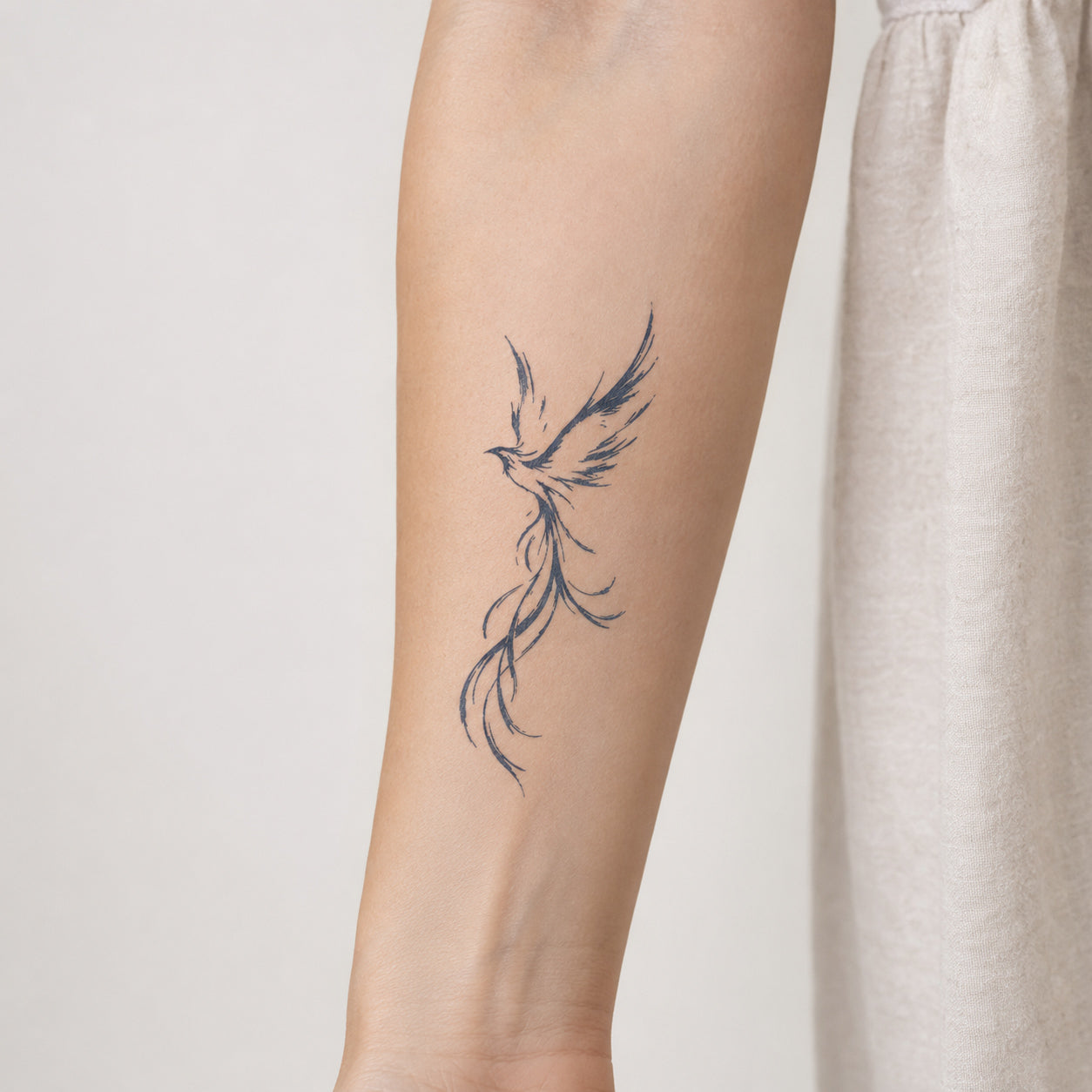 Delicate phoenix bird tattoo with flowing feather details placed on a woman’s forearm, featuring an elegant phoenix temporary tattoo design.