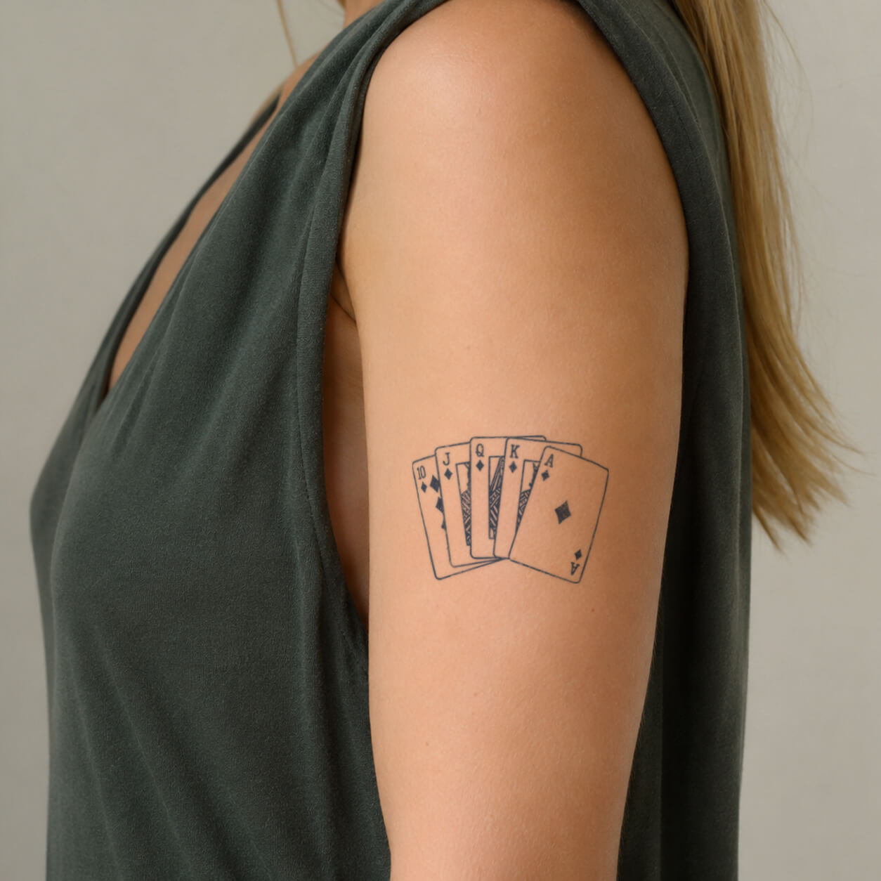 Close-up of a playing card tattoo featuring a fan of poker cards with diamond suits and detailed line work on the upper arm. This casino inspired temporary tattoo design creates a bold yet minimalist style for card game lovers.