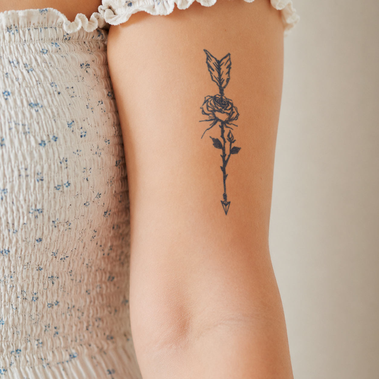 Flower temporary tattoo featuring a blooming rose pierced by a delicate arrow on the upper arm.