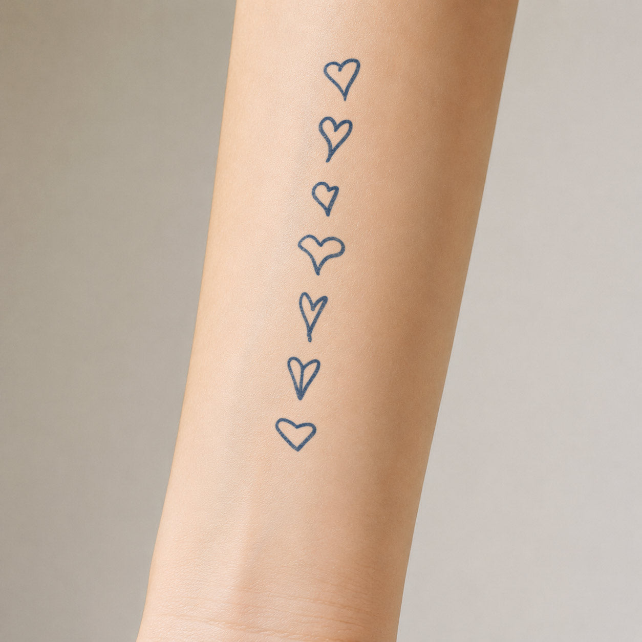 Temporary forearm tattoos featuring seven hand-drawn outline hearts arranged in a vertical row.

