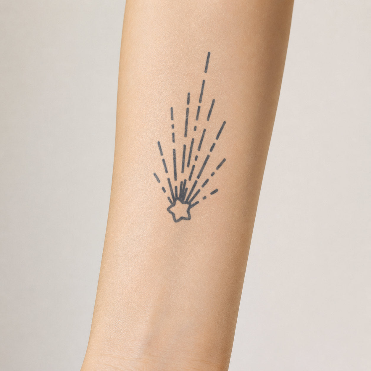 Small star semi-permanent tattoo of a shooting star with long radiating trails on the inner forearm.