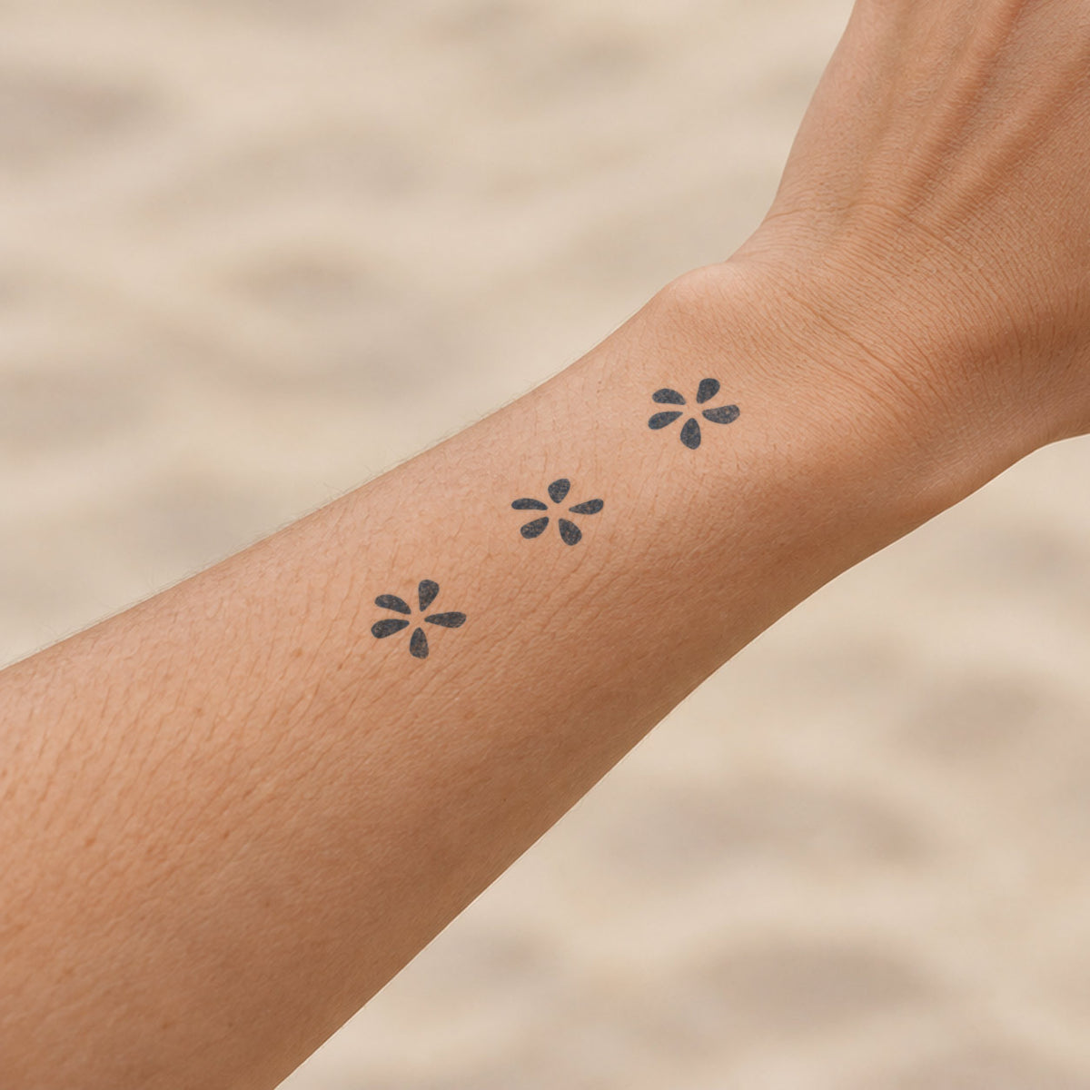 Floral temporary tattoos featuring three small minimalist five-petal flowers in blue-black ink along the forearm near the wrist.