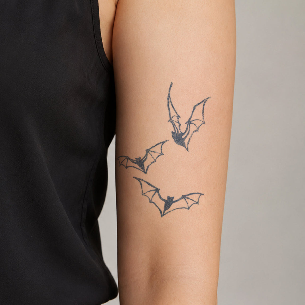 Temporary tattoo designs featuring three flying bats in blue-black line art on the upper arm.