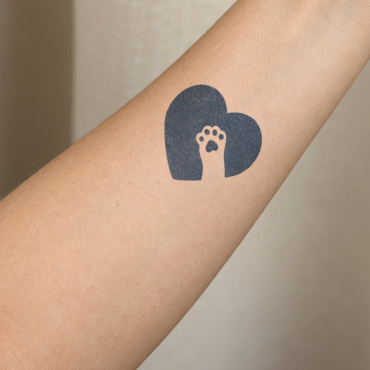 Minimalist temporary tattoos featuring a paw print inside a bold heart shape in blue-black ink on the forearm.