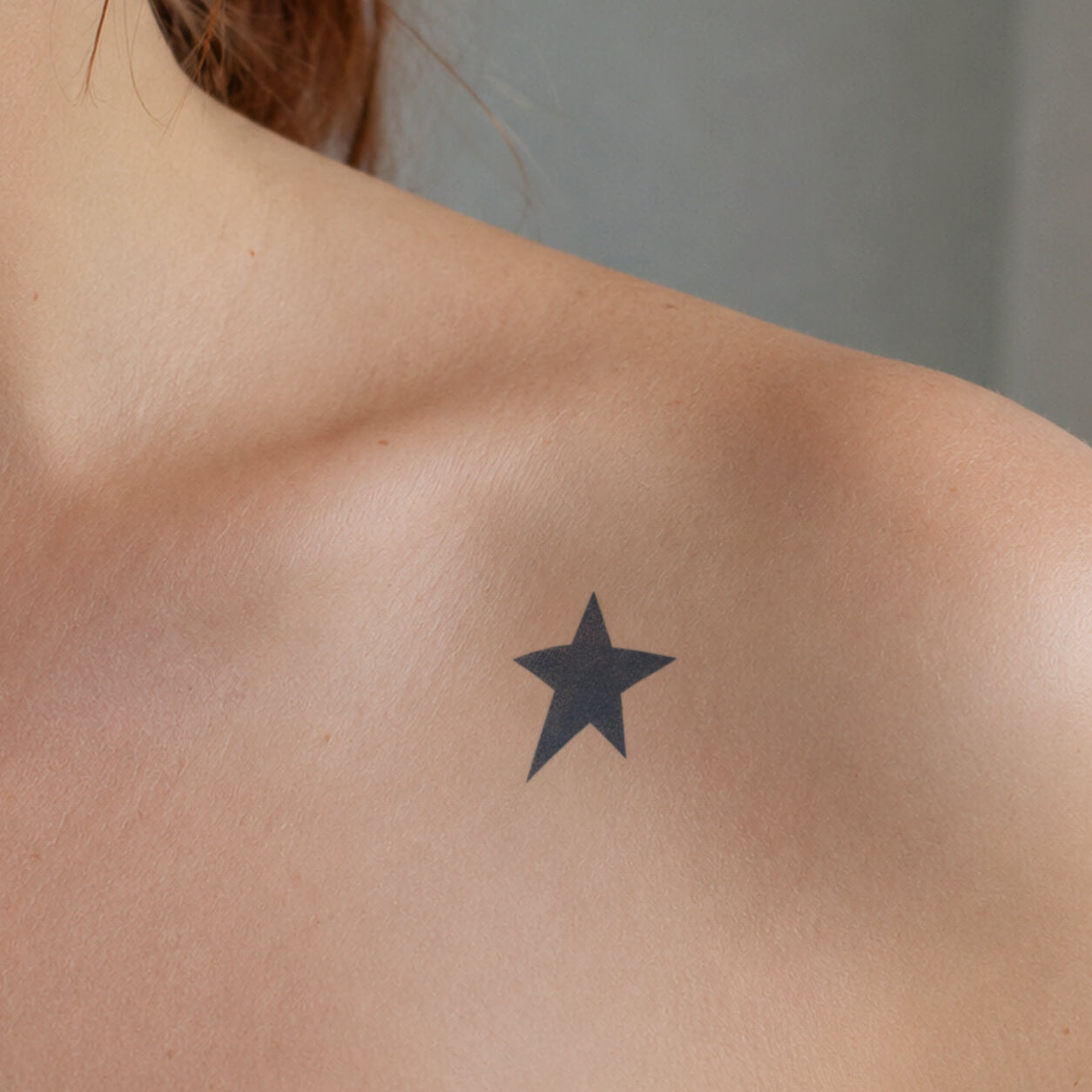 Solid black star temporary tattoo sticker placed below the collarbone, creating a simple bold chest design with clean edges.