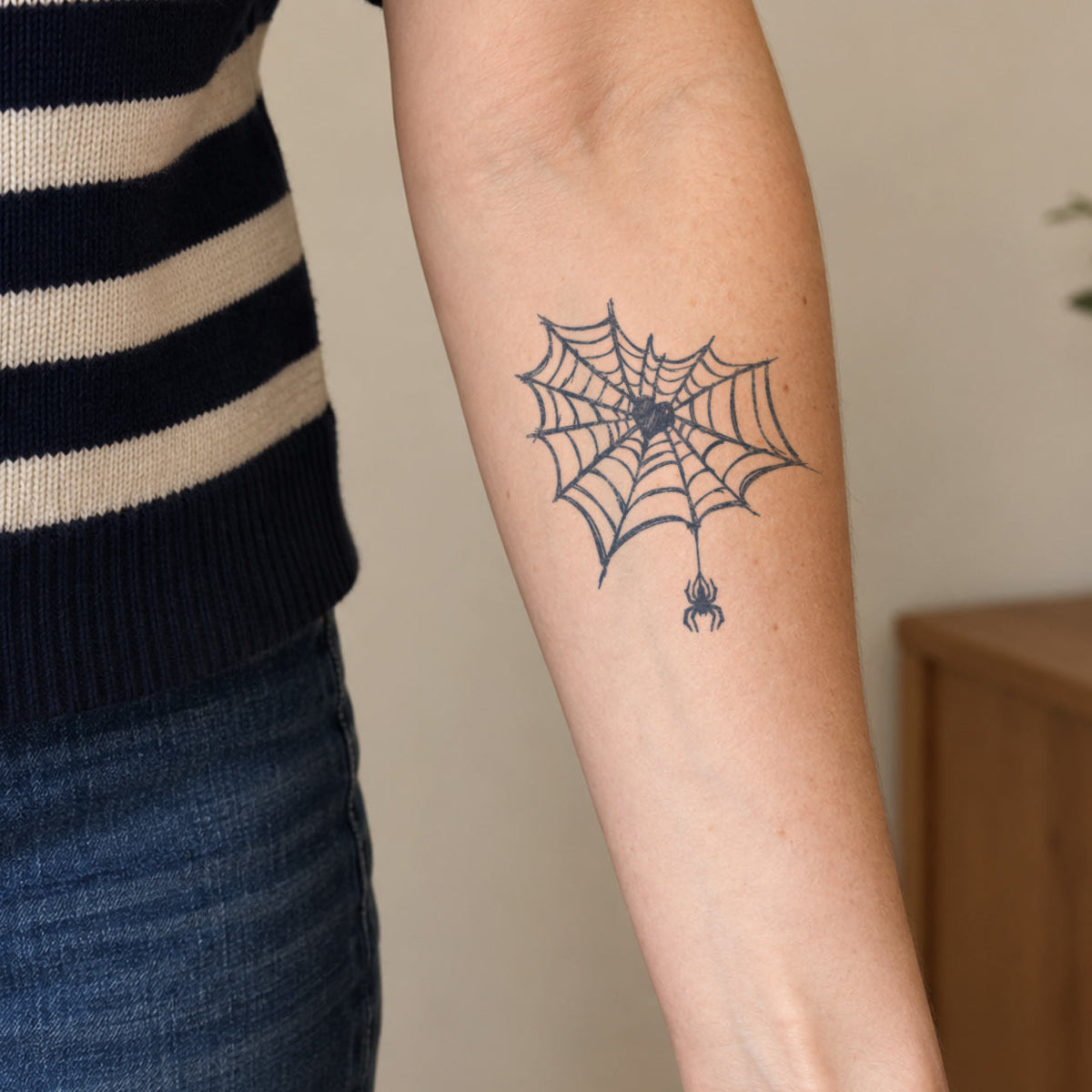 Temporary tattoo designs featuring a detailed spider web with a small hanging spider in blue-black ink on the inner forearm.