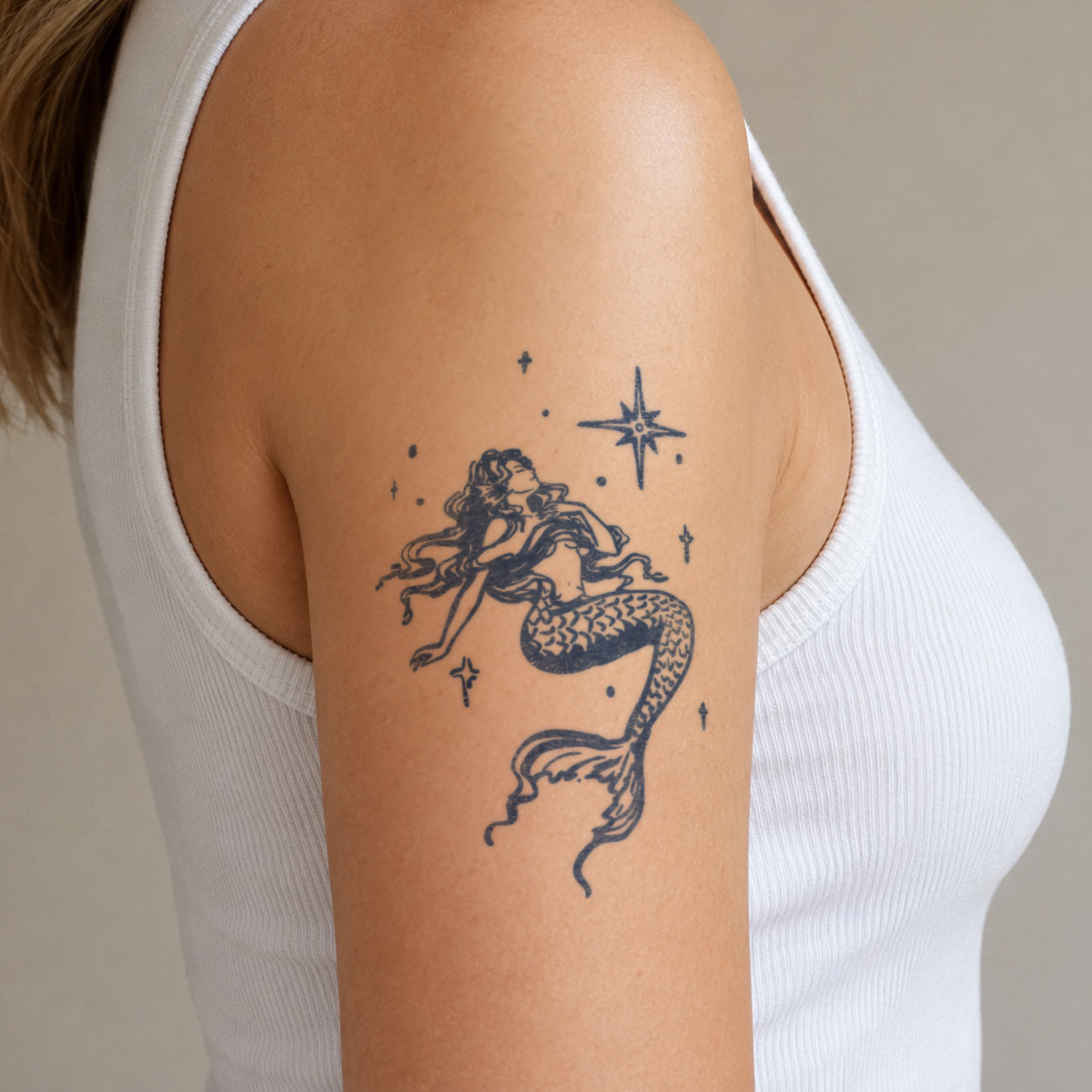 Detailed semi-permanent tattoo featuring a graceful mermaid surrounded by tiny stars on the upper arm.