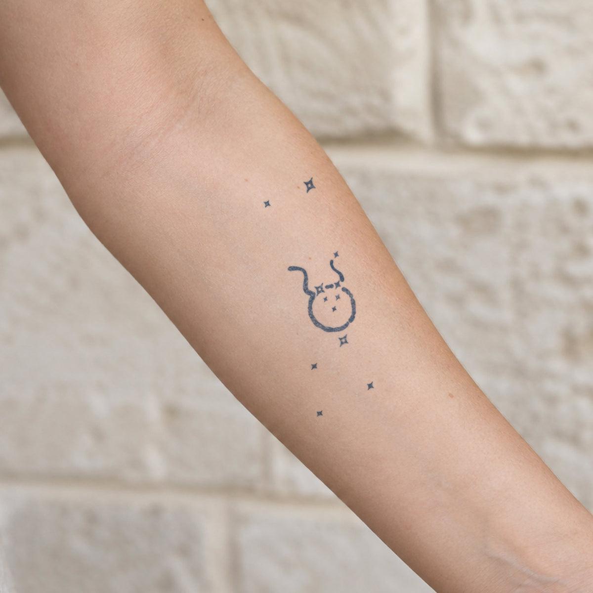 Aesthetic temporary tattoos featuring a minimalist Taurus zodiac symbol surrounded by small sparkling stars in blue-black ink.