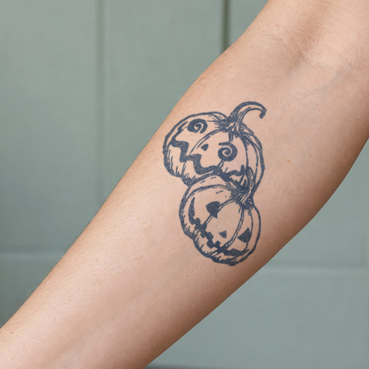 Temporary tattoo designs featuring two Halloween jack-o’-lantern pumpkins in blue-black ink on the forearm