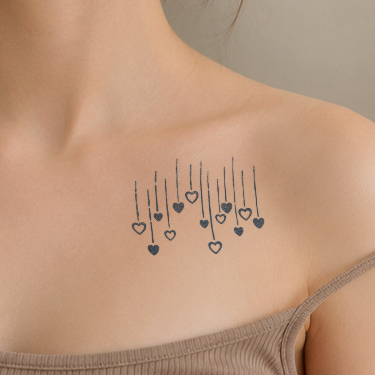 Small temporary tattoos featuring delicate hanging hearts and fine vertical lines arranged across the collarbone in blue-black ink.