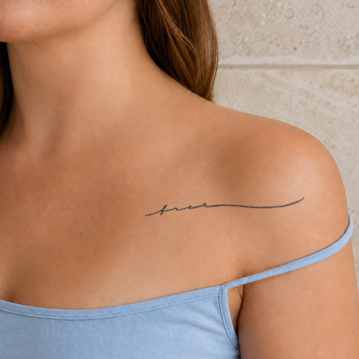 Temporary script tattoos featuring a delicate cursive word design along a woman’s collarbone in blue-black ink.