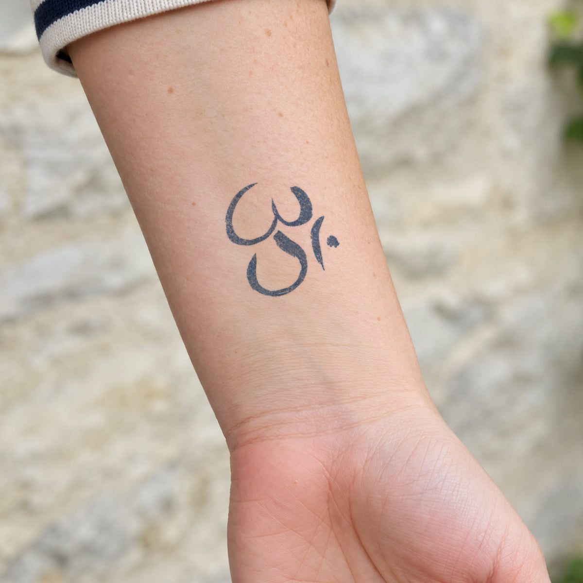 Temporary wrist tattoos featuring a minimalist Om symbol in blue-black ink on the inner wrist.