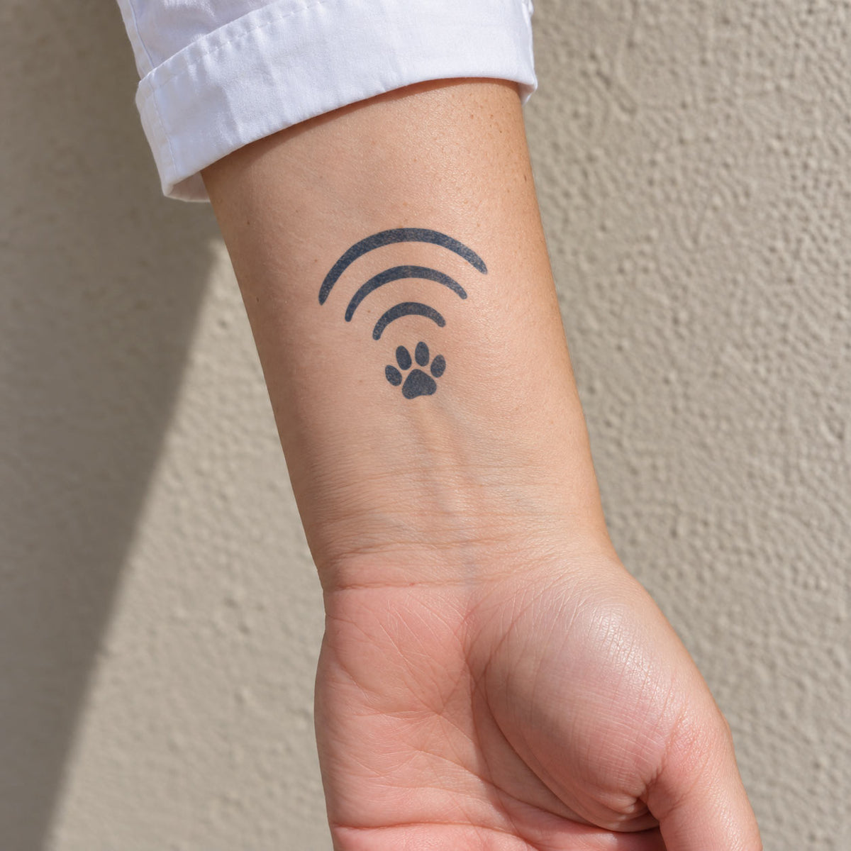 Small temporary tattoos featuring a paw print beneath curved signal lines in blue-black ink on the inner wrist.