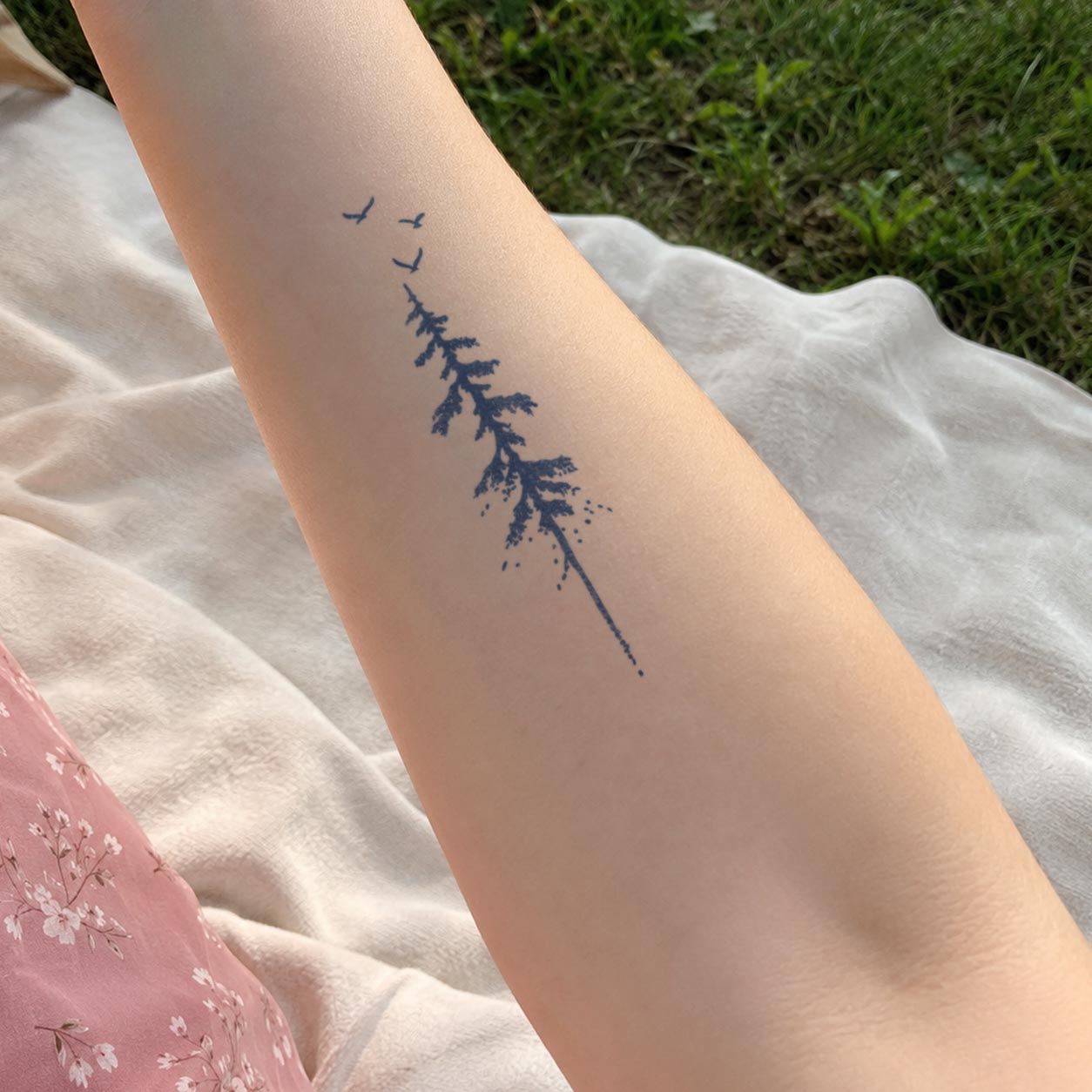Semi-permanent tattoo featuring a slender tree with small birds flying above it on the inner forearm.