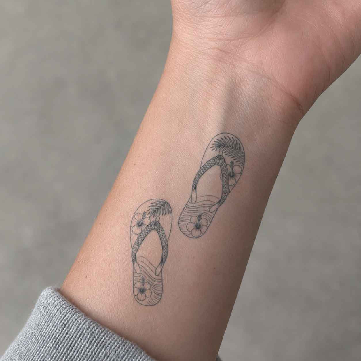 Beach temporary tattoo applied on wrist with tropical flip-flops and hibiscus flower line art design.