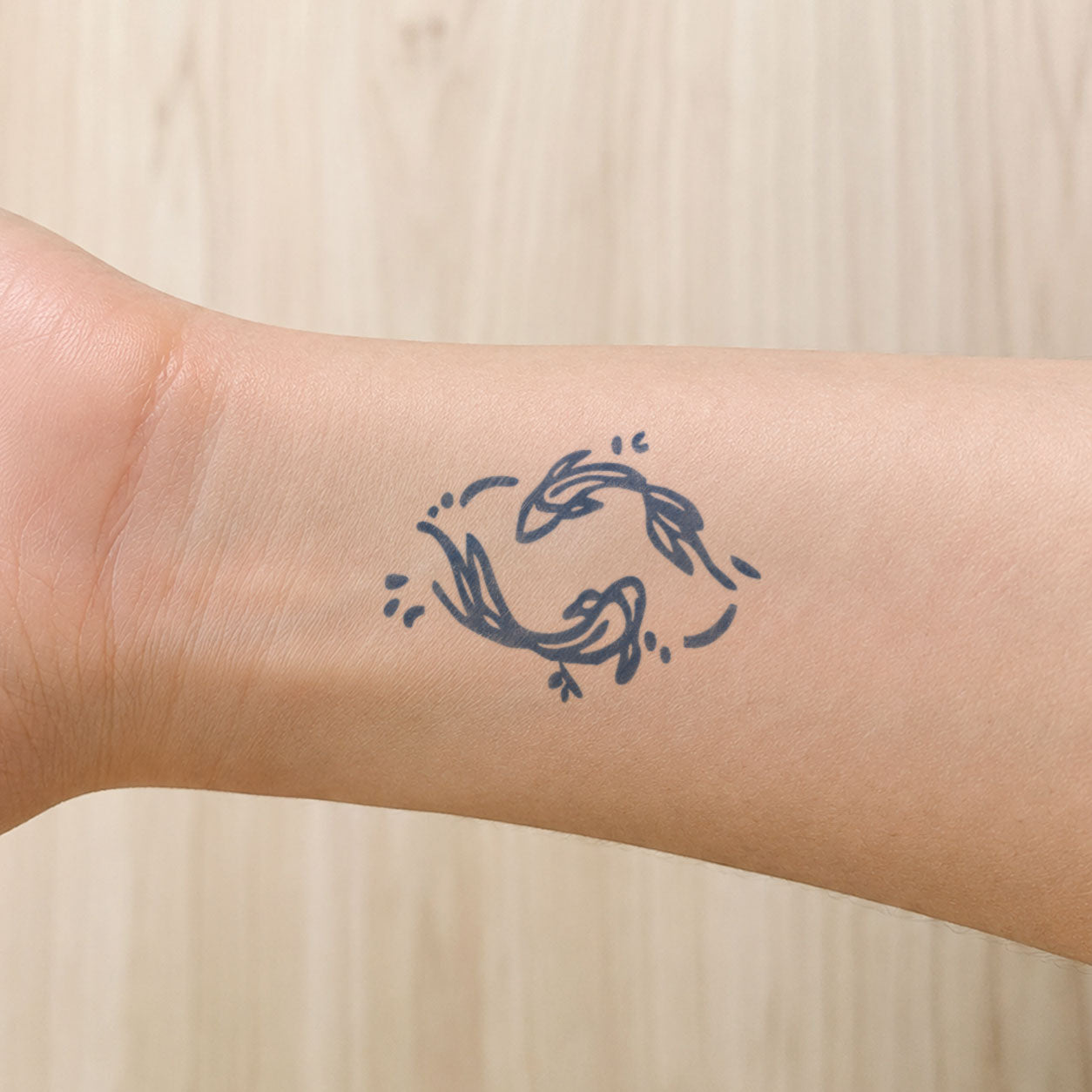 Temporary wrist tattoos featuring two small fish swimming in a circular design with playful wave-like accents.