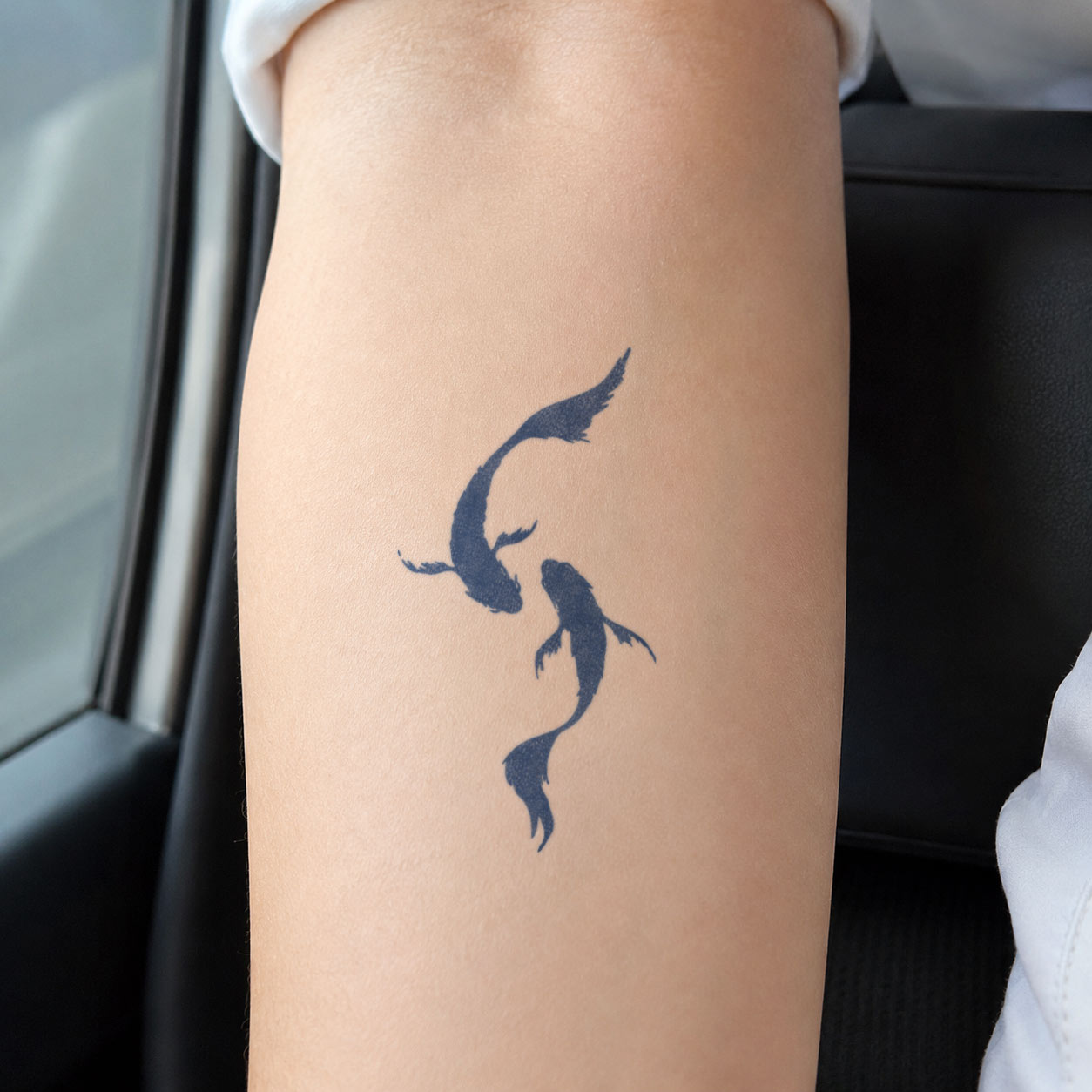 Semi-permanent tattoo showing two graceful koi fish circling one another in a fluid, balanced design on the upper arm.