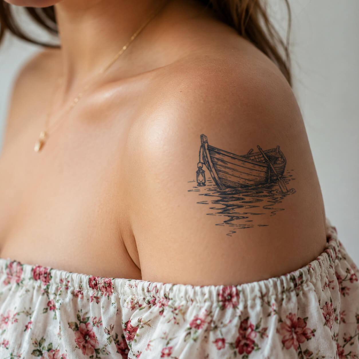 Vintage wooden boat temporary tattoo featuring a small lantern, calm water reflections, and hand-drawn waves on the shoulder with a coastal nautical style