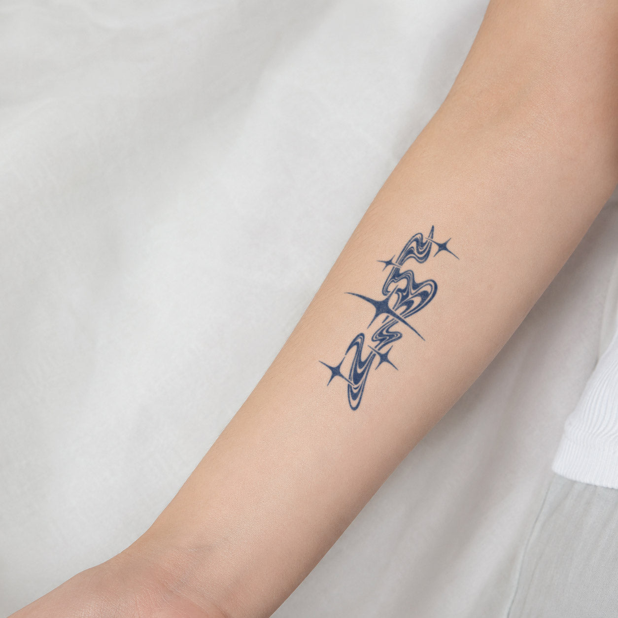 A simple temporary tattoo with a soft concentric water ripple pattern, adorned with stars, on the inside of the forearm.