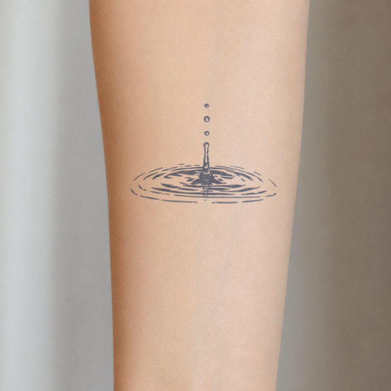 Minimal semi-permanent tattoo design of a falling water droplet creating soft circular ripples on the forearm.