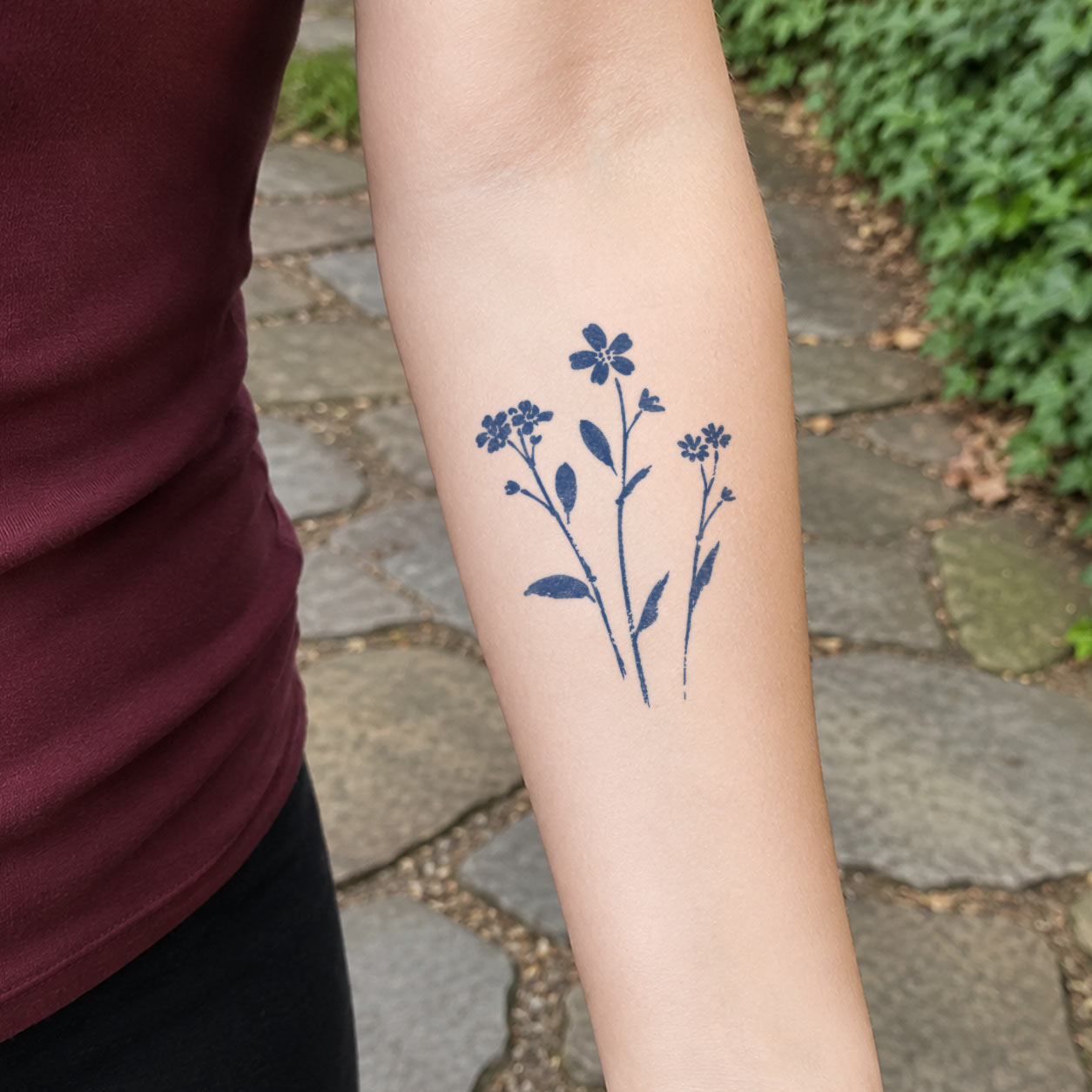 Flower temporary tattoo depicting three simple wildflower stems with tiny blooms and leaves on the forearm.