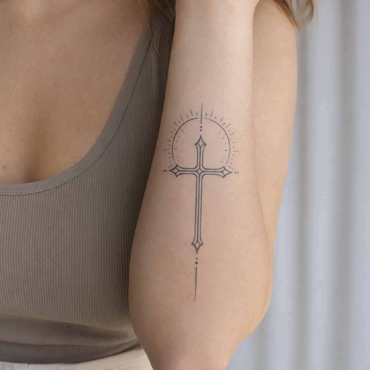 Woman wearing minimalist cross semi-permanent tattoo on upper arm