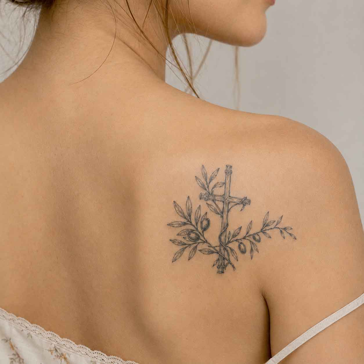 Woman wearing olive branch cross semi-permanent tattoo on upper back shoulder