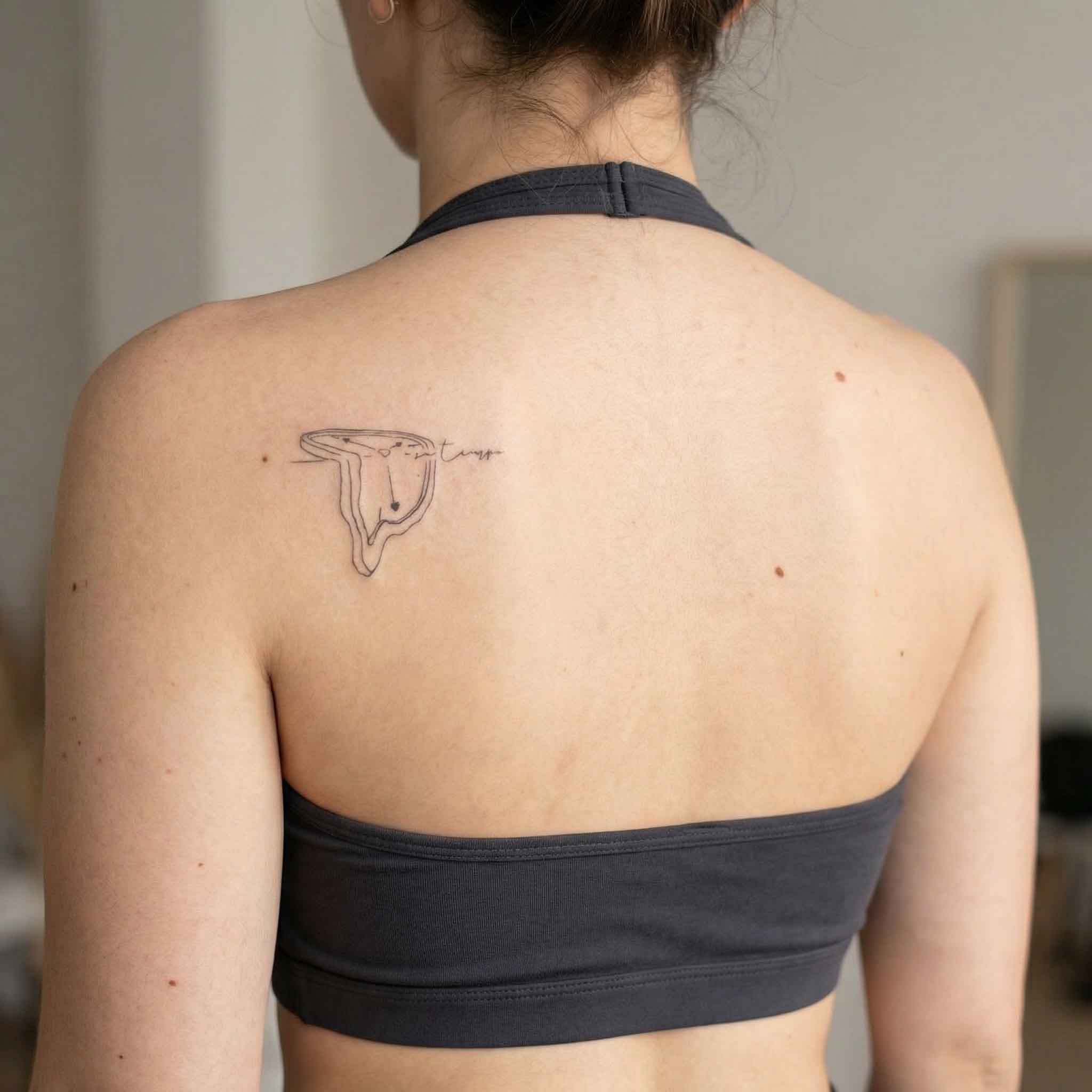 Surreal clock tattoo worn on the back with simple word detail