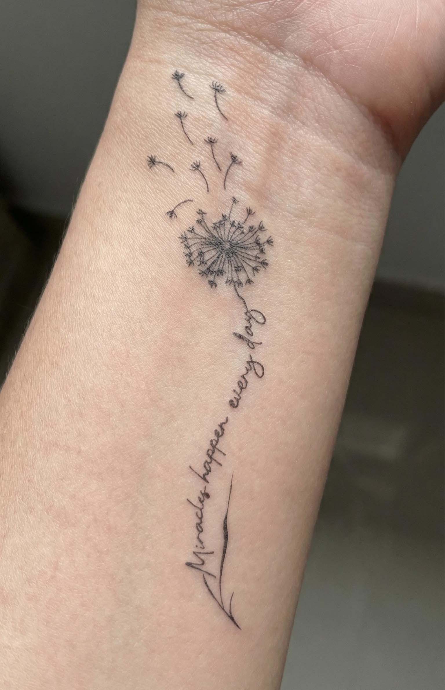 fine line dandelion temporary tattoo with script "miracles happen every day" minimalist wrist tattoo design