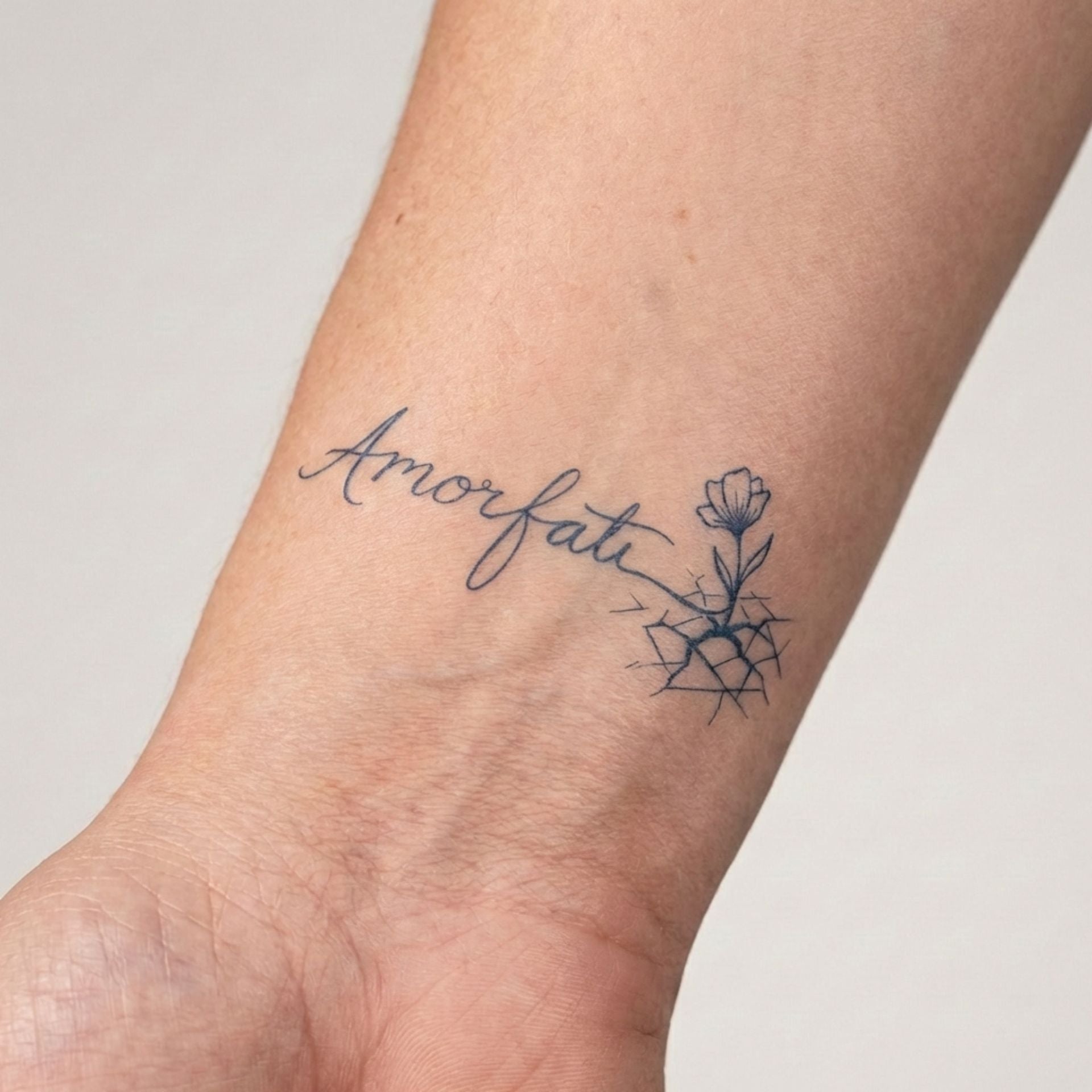 Minimal script flower tattoo worn on the wrist with delicate botanical details