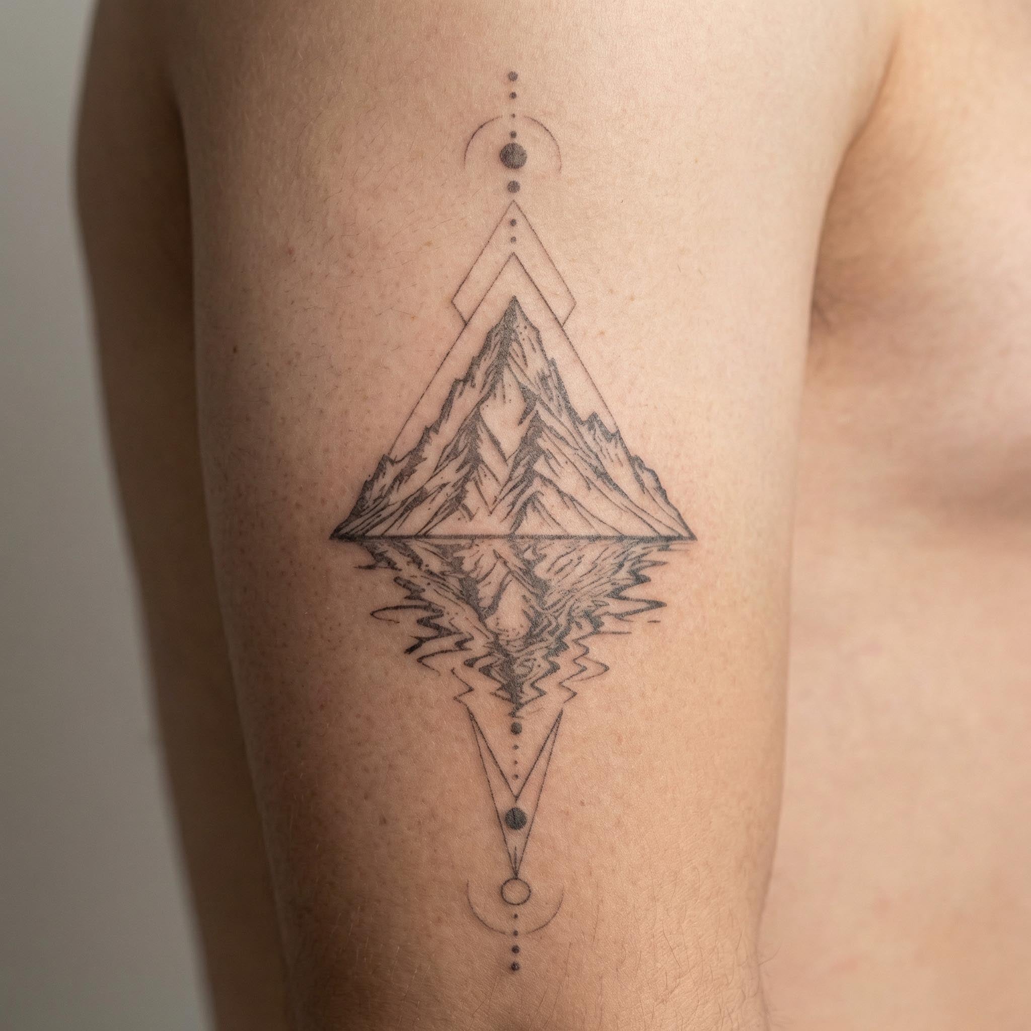 Mountain reflection tattoo worn on forearm with geometric line art style