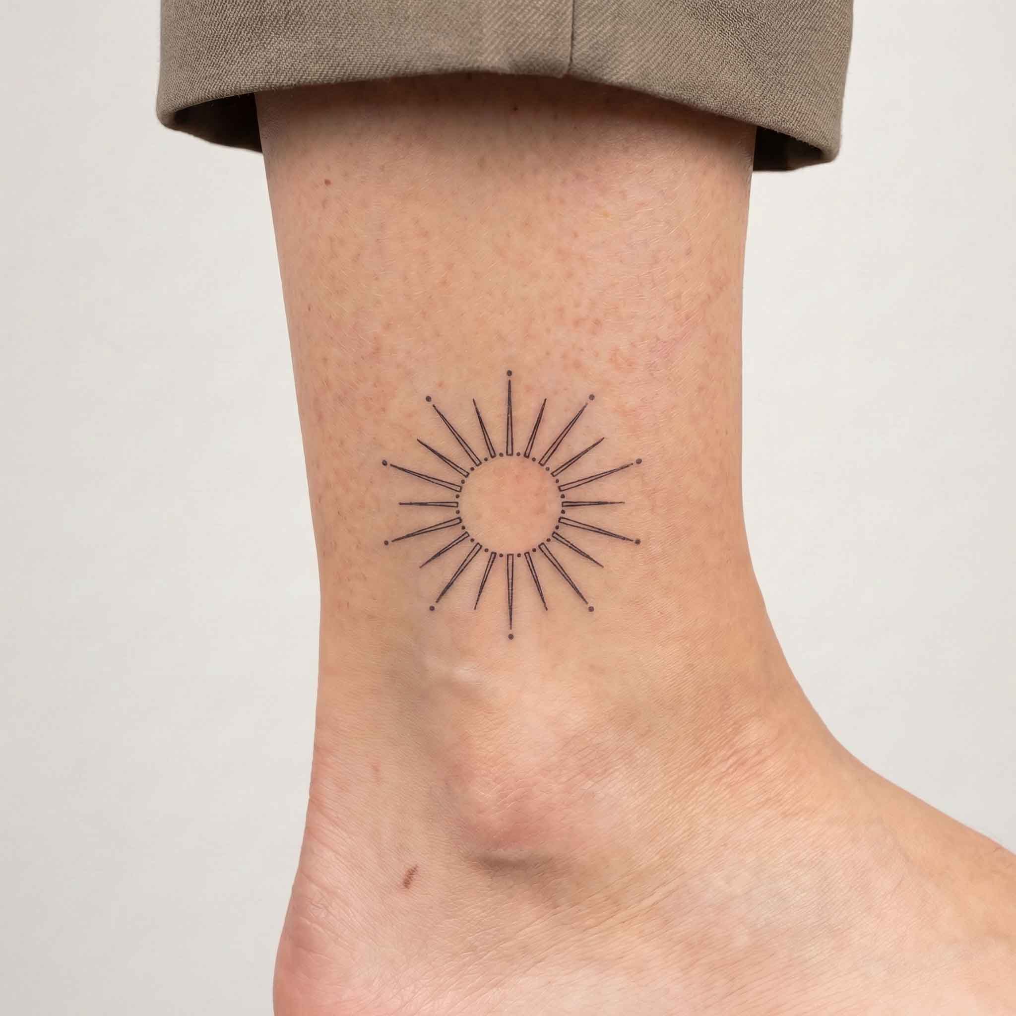 Minimalist geometric sun tattoo worn on ankle in fine line style