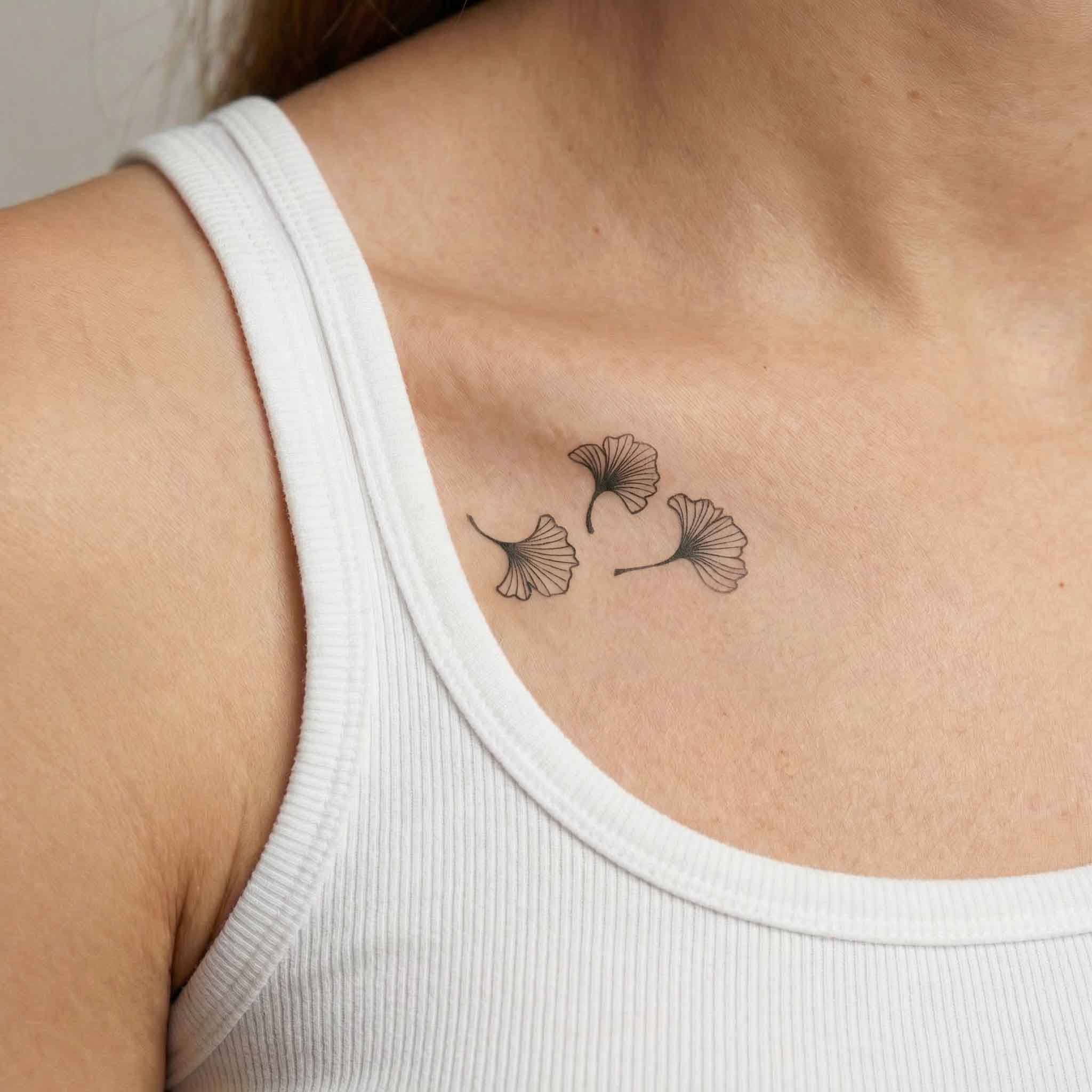 Minimal ginkgo leaf tattoo worn on the clavicle with soft nature-inspired lines