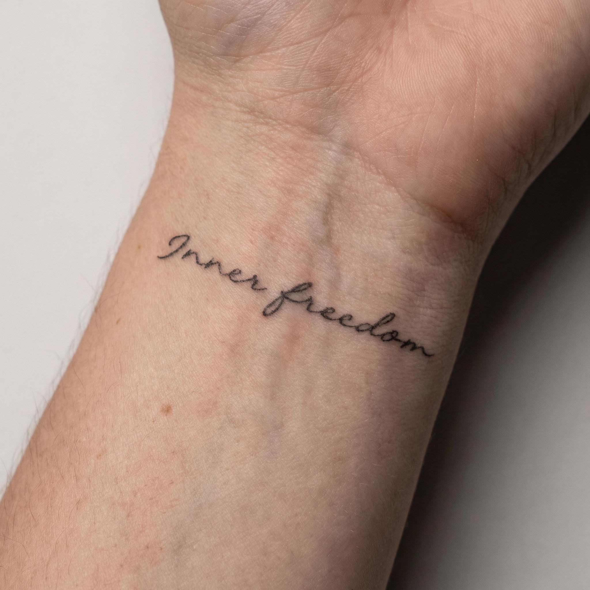 Fine line inner freedom word fake tattoo placed on wrist