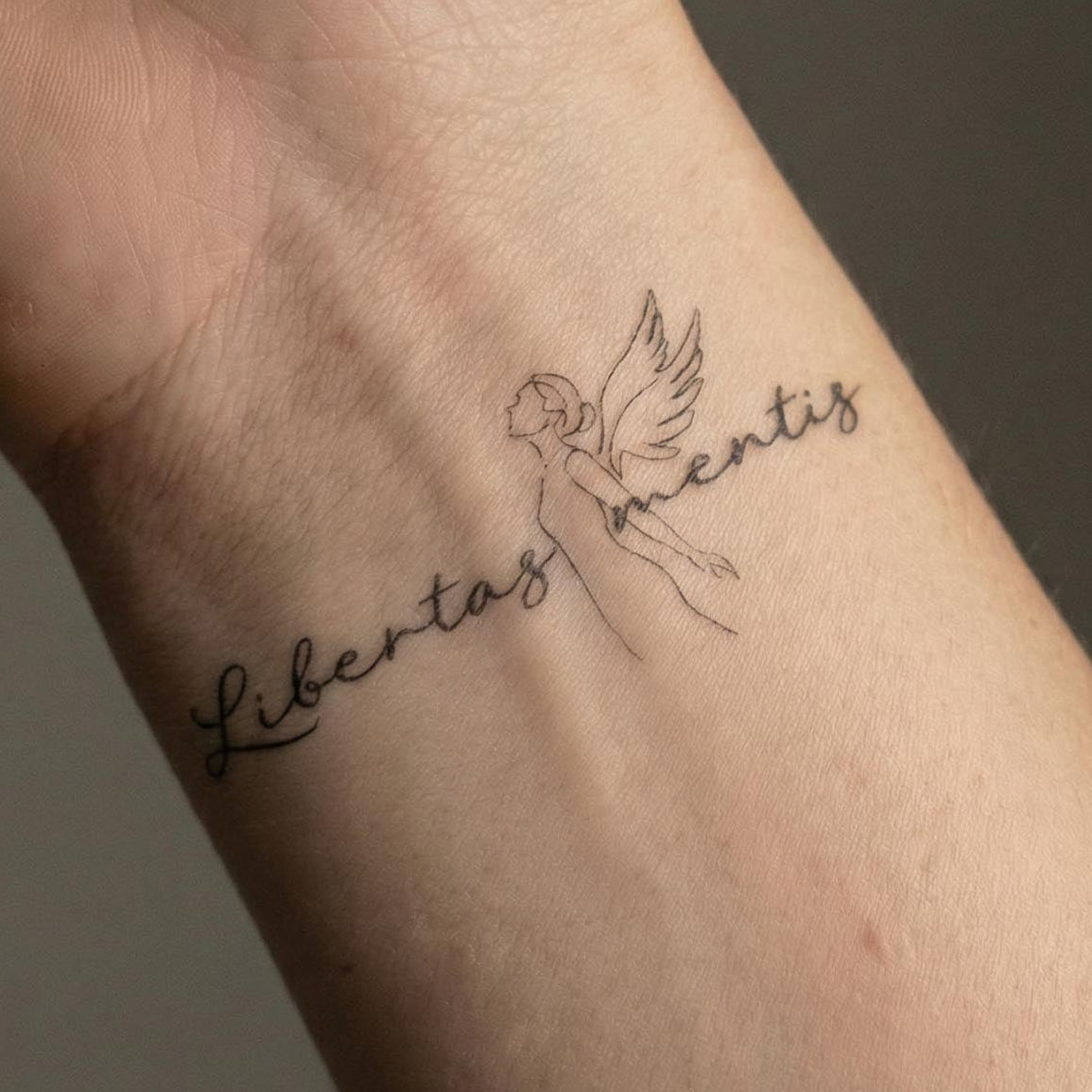 fine line angel temporary tattoo with latin text "libertas mentis" minimalist wrist tattoo design