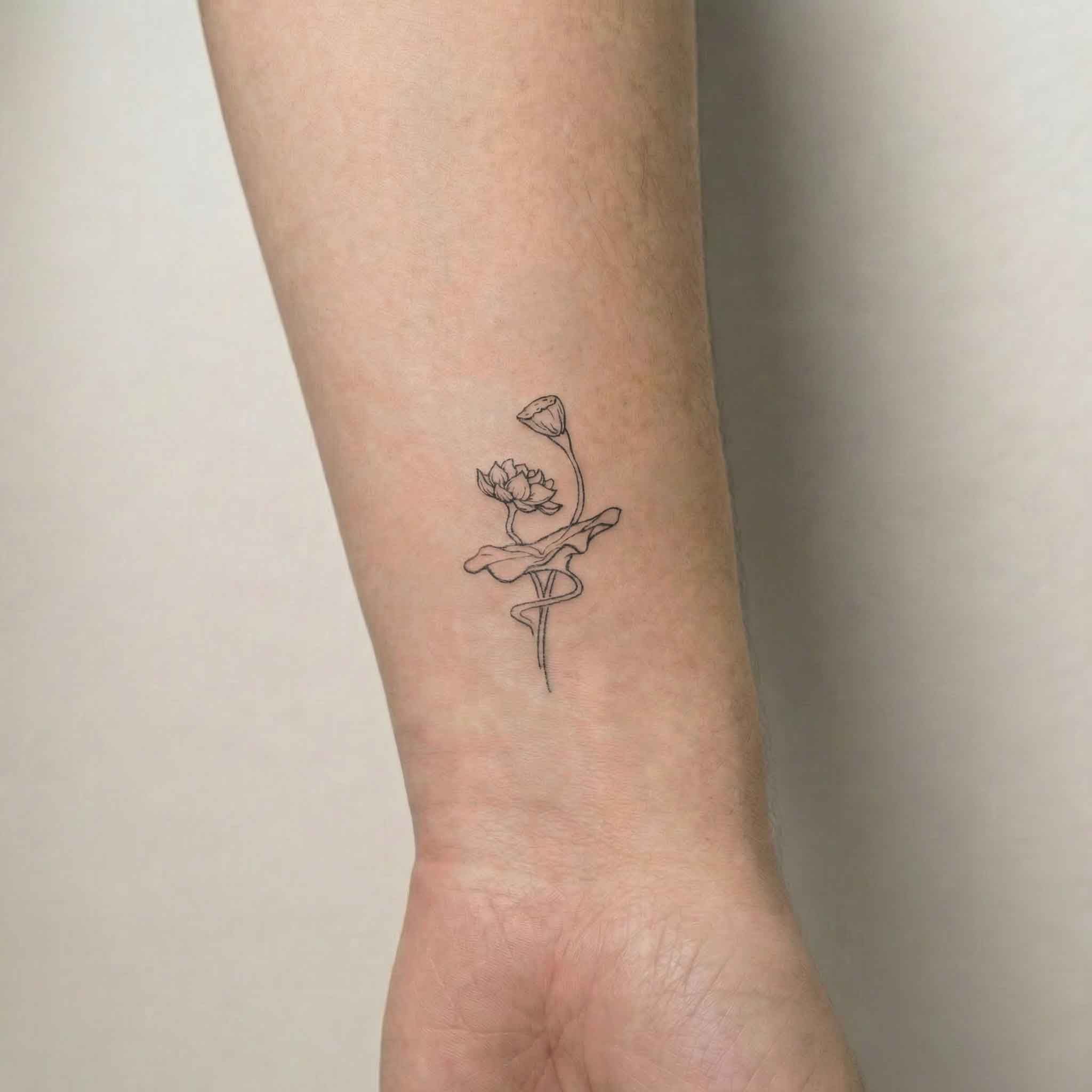 Minimal lotus tattoo on wrist with soft botanical details