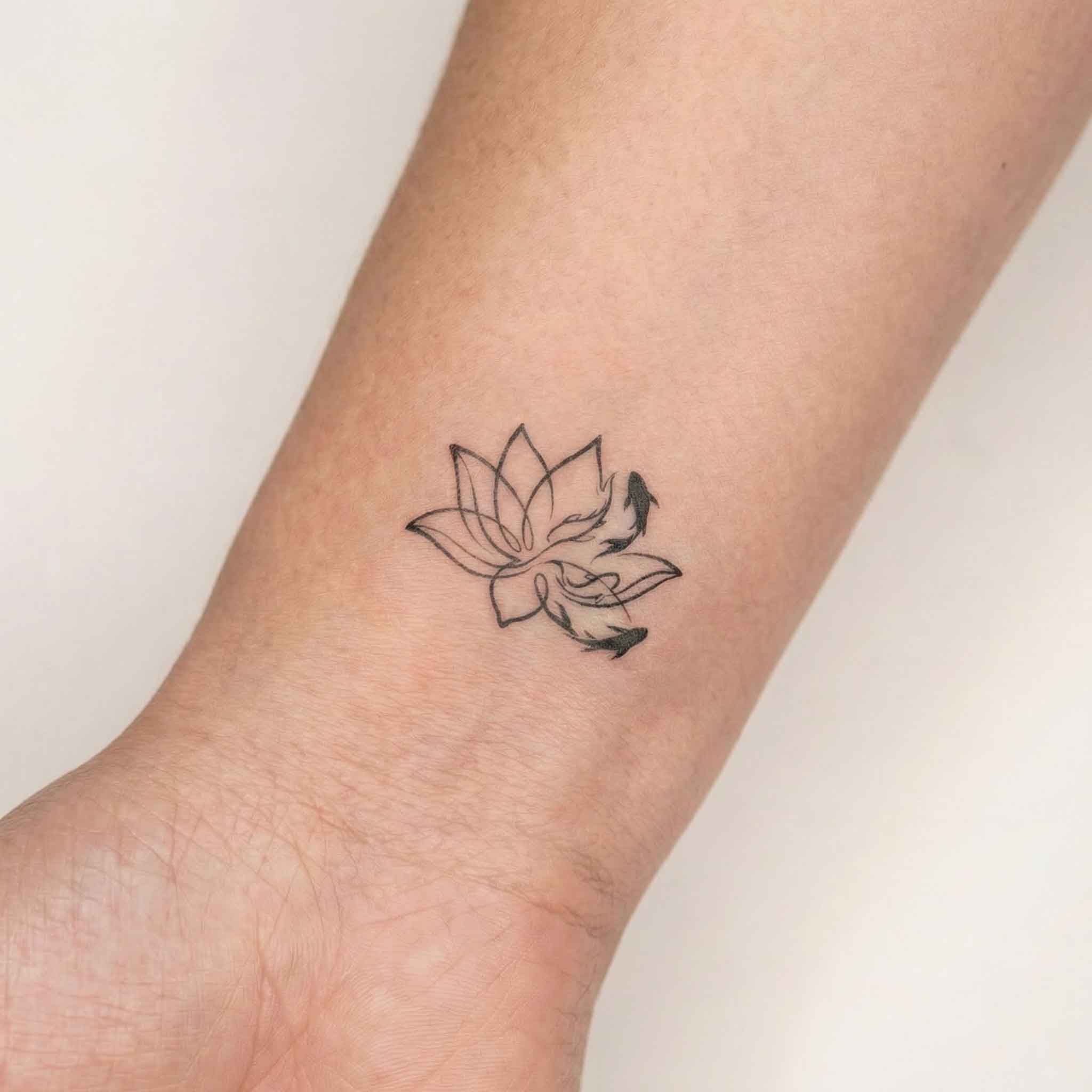 Minimal koi fish temp tattoo worn on the wrist with lotus flower linework