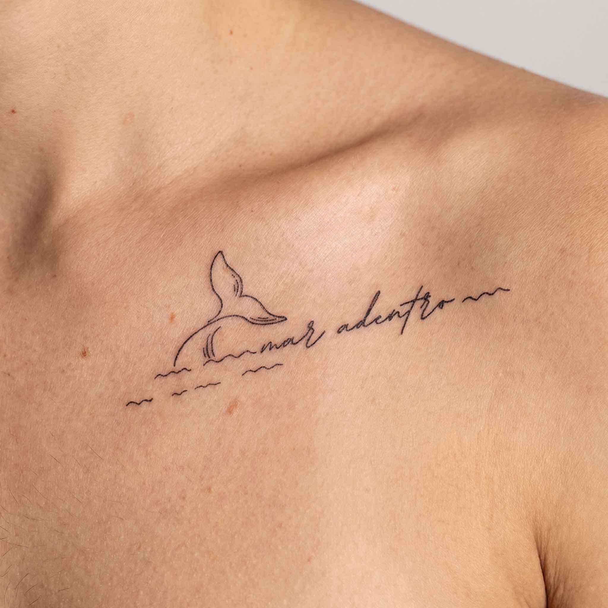Minimal whale tail tattoo worn on the clavicle with clean sea-inspired detail