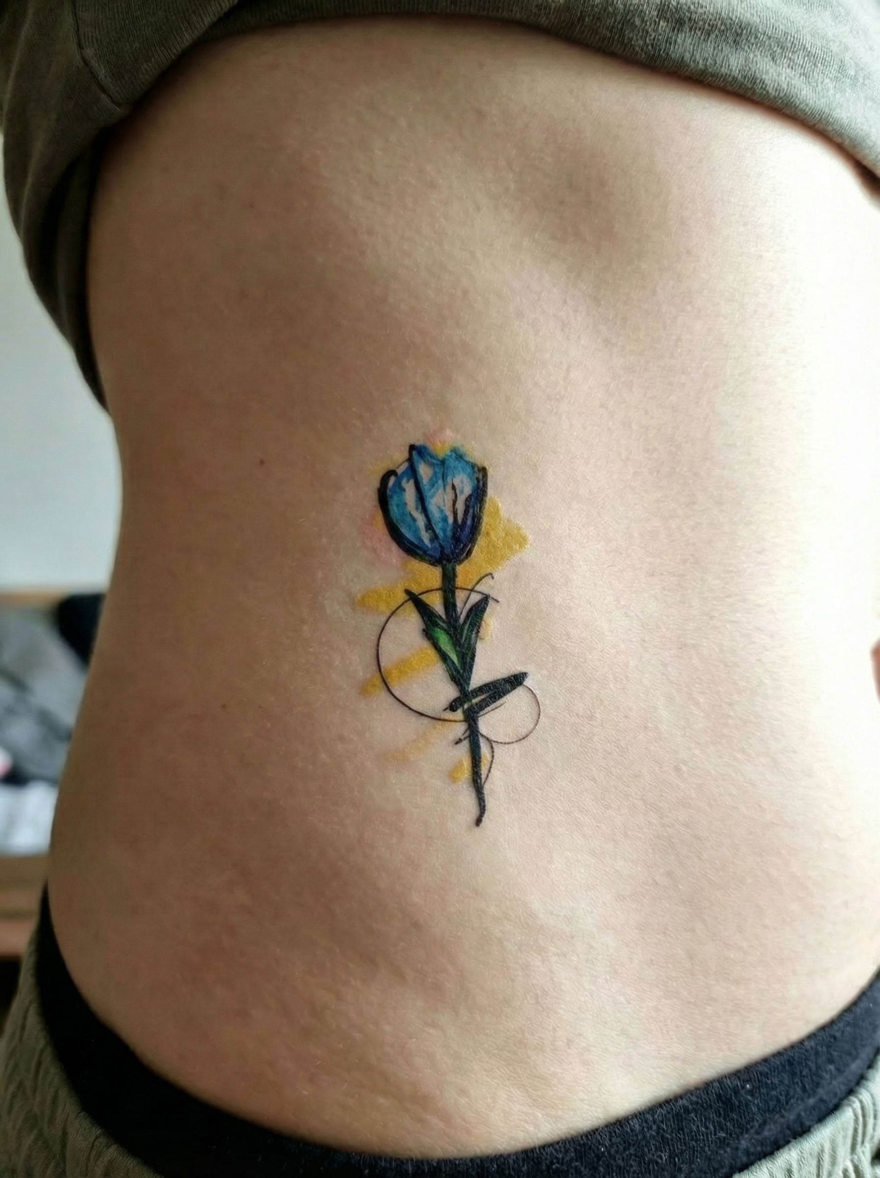 Matte blue flower temporary tattoo on rib, artistic floral semi-permanent tattoo with fine lines and soft watercolor accents