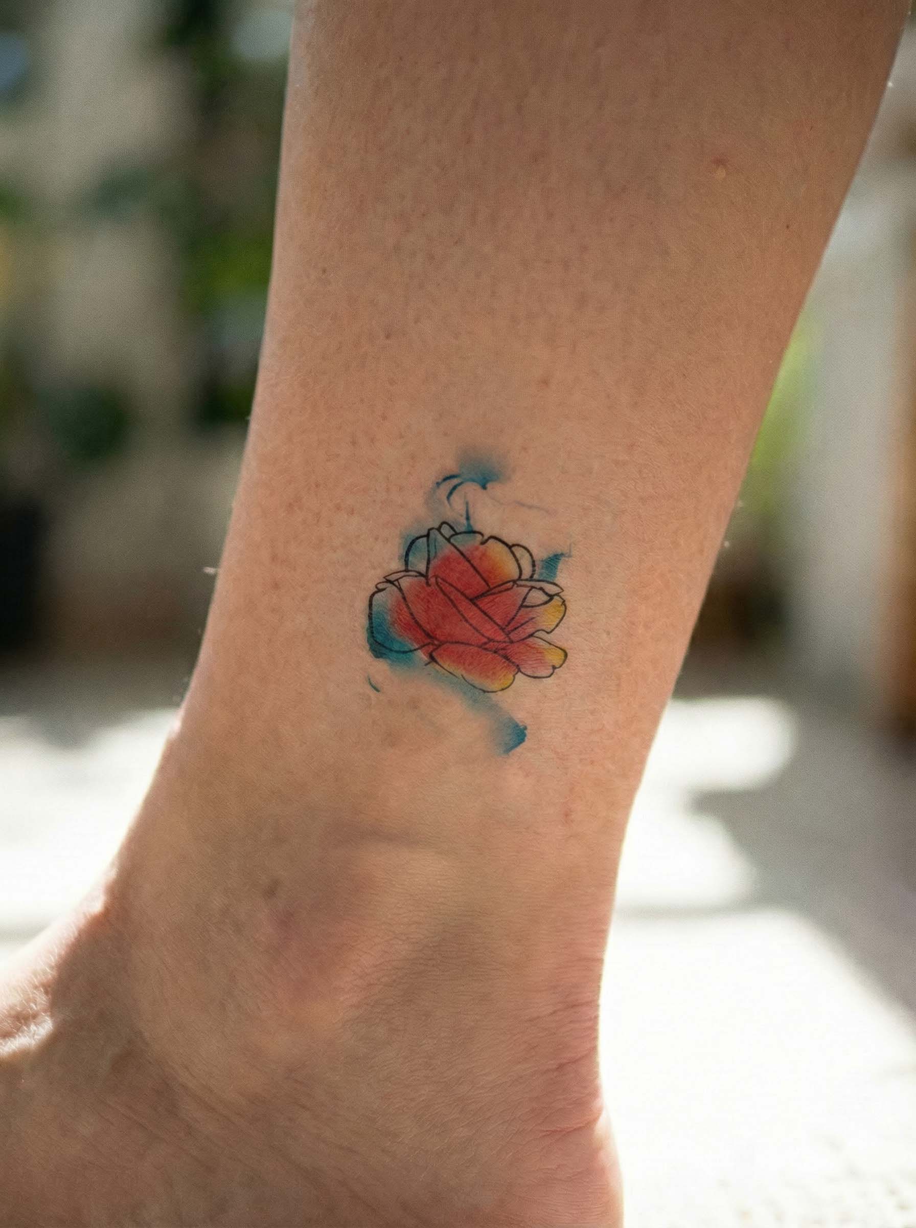 Matte watercolor rose temporary tattoo on ankle, artistic floral semi-permanent tattoo with soft blue and warm orange tones