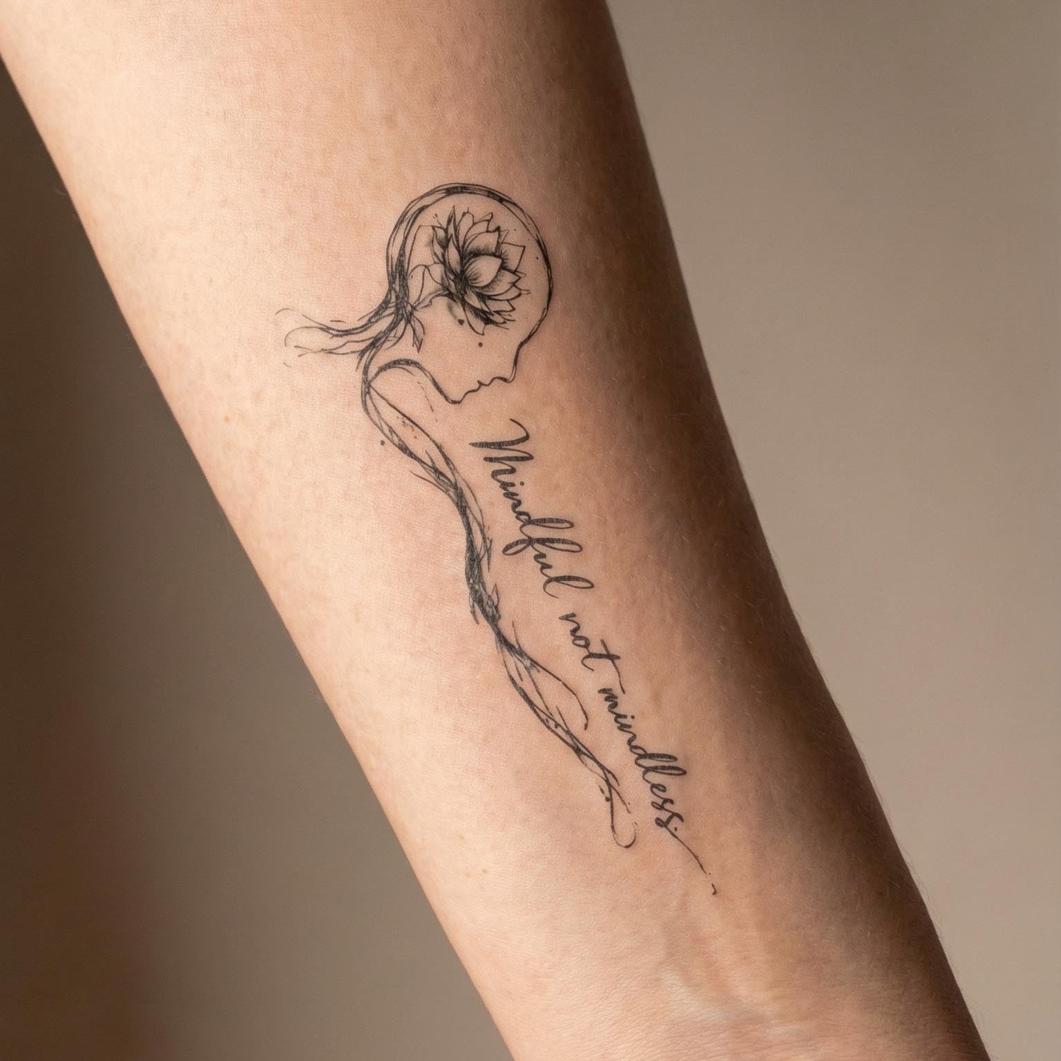 fine line woman head flower temporary tattoo with text "mindful not mindless" minimalist tattoo design on arm